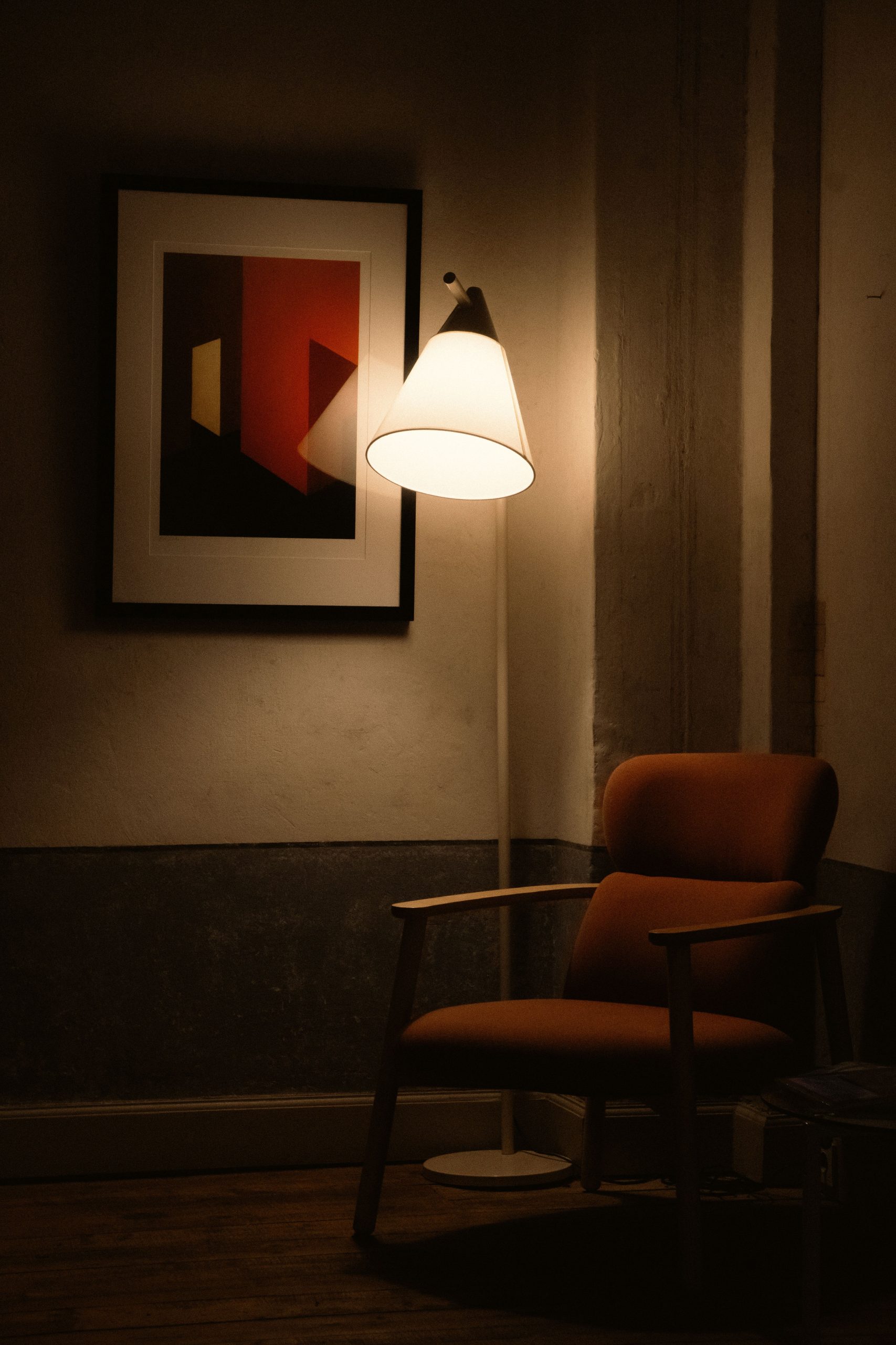 A warm, inviting corner featuring a modern armchair, floor lamp, and abstract art.