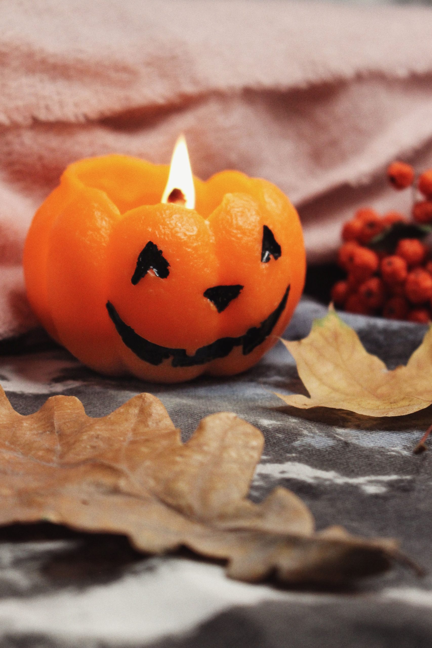 A warmly lit Jack-o'-Lantern candle next to autumn leaves, perfect for Halloween decor.
