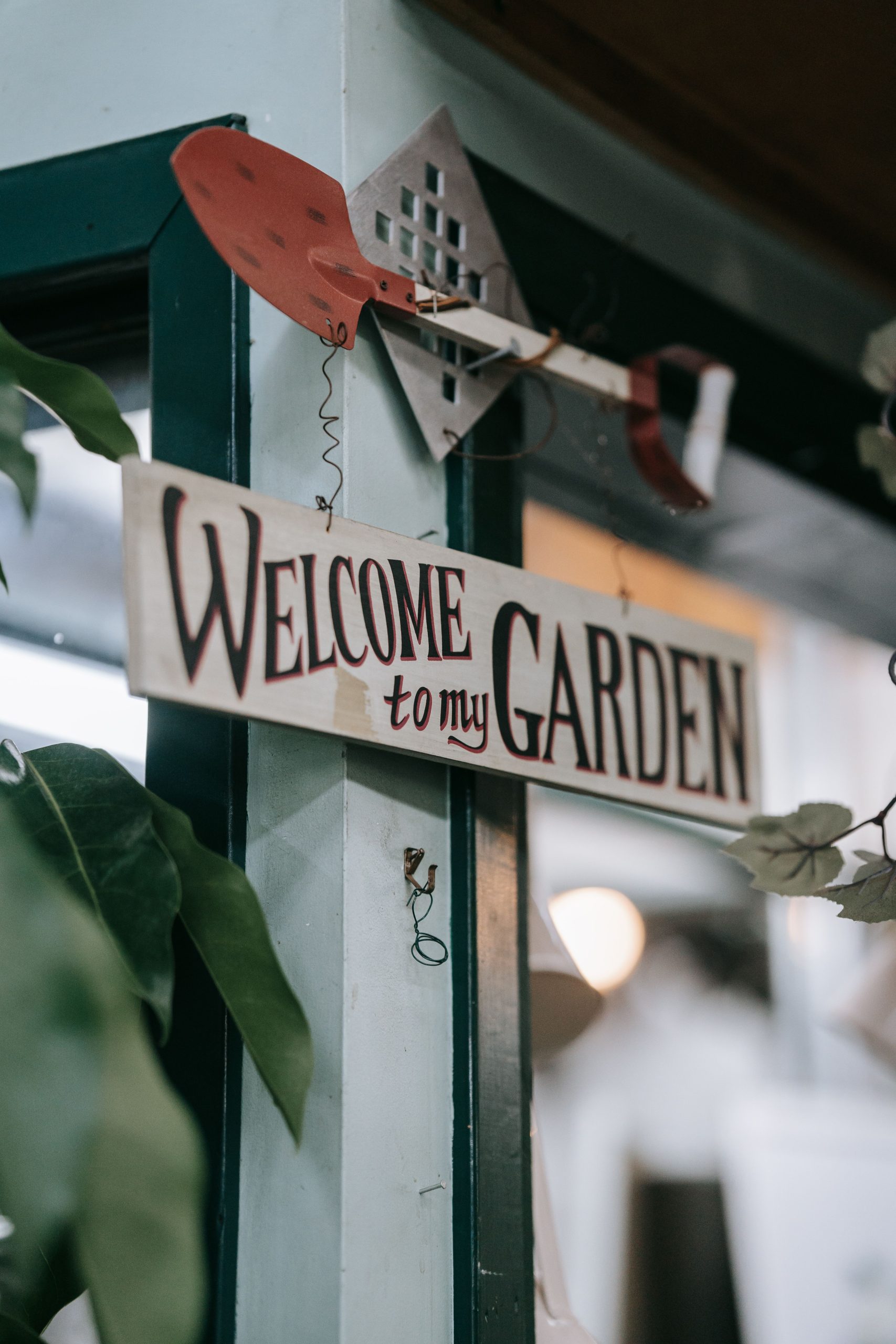 A welcoming garden sign with decorative shovel accent, perfect for outdoor spaces.