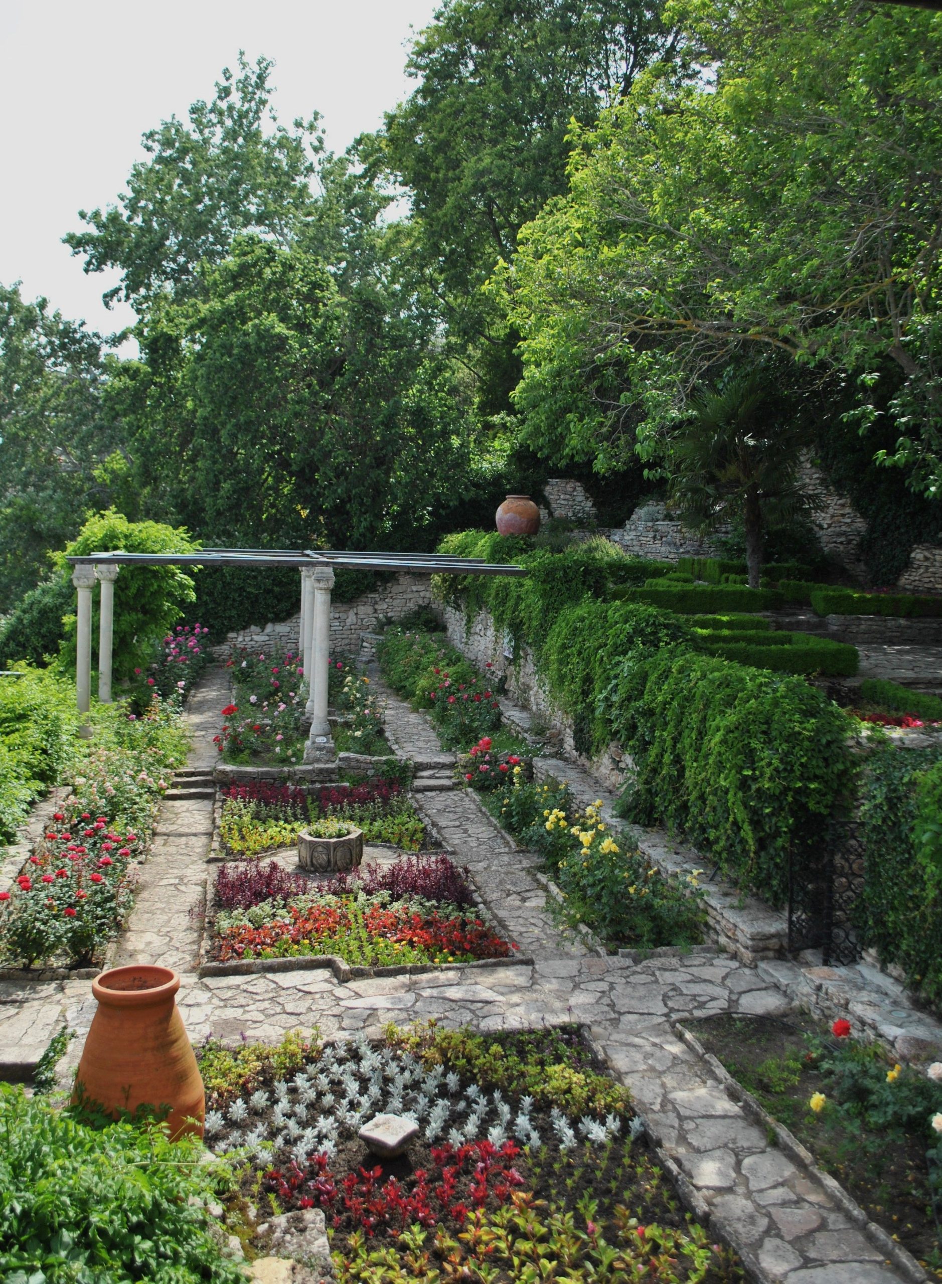 Beautiful tiered Mediterranean garden with vibrant flowers and lush greenery under a bright day.