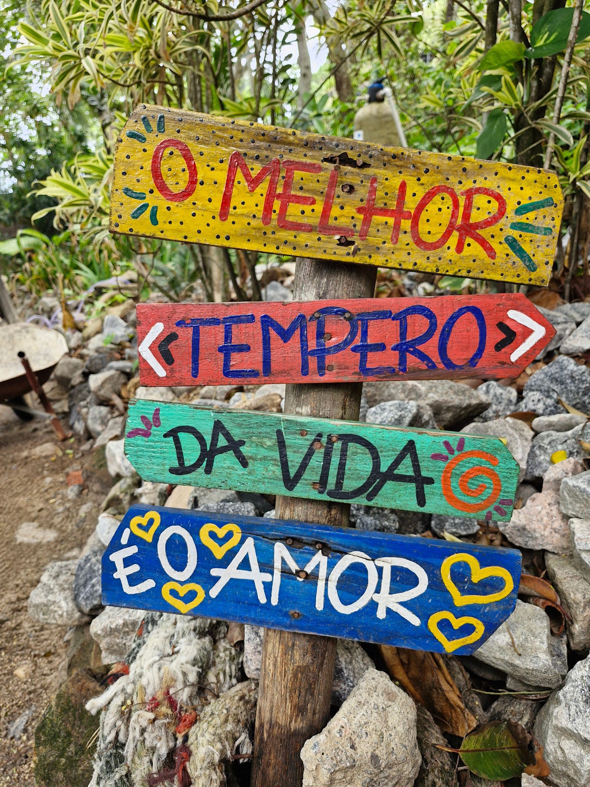 Bright, hand-painted sign offering an inspiring message set among garden rocks and plants.
