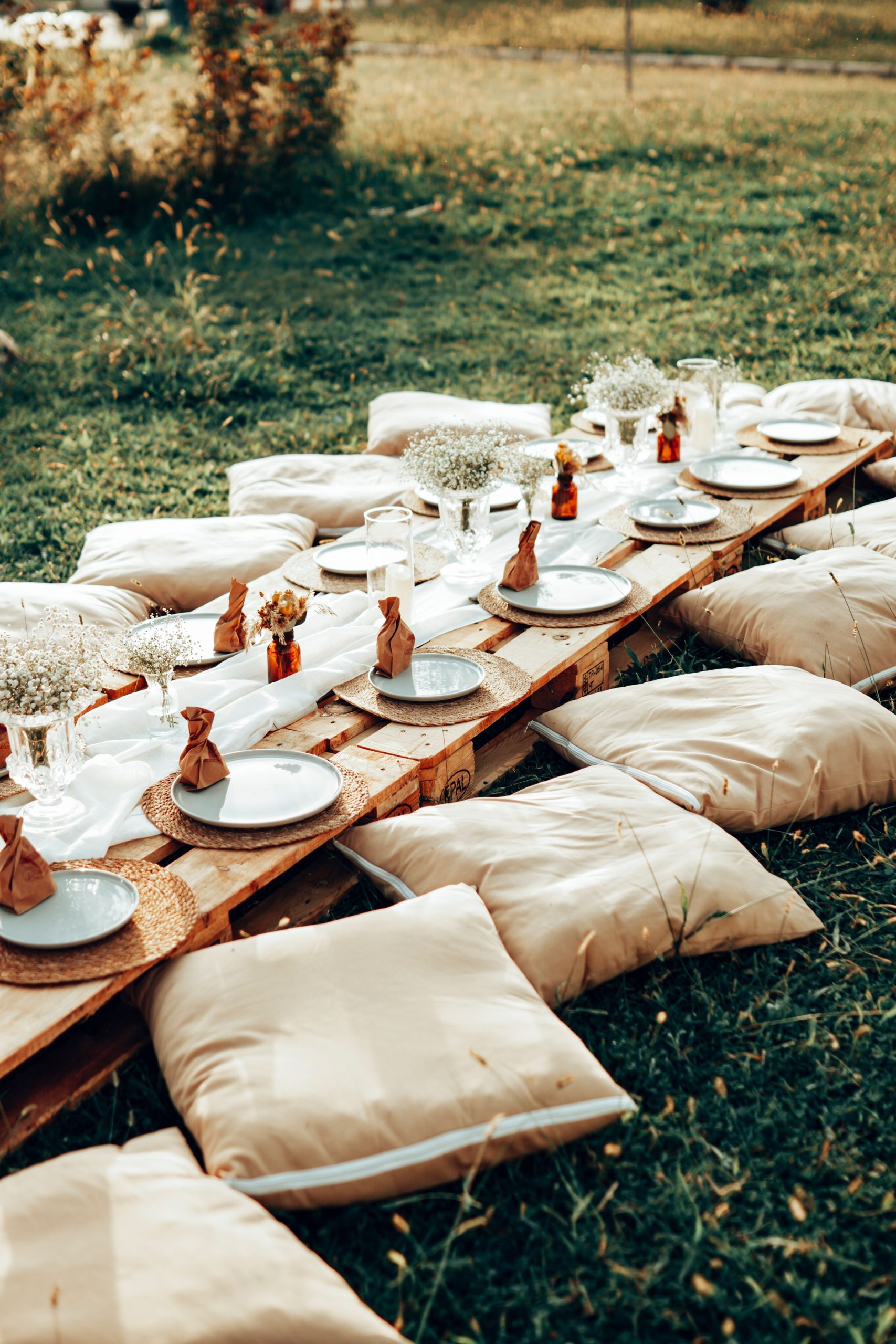 Charming outdoor picnic setup with cushions and rustic wooden pallets in a grassy field.