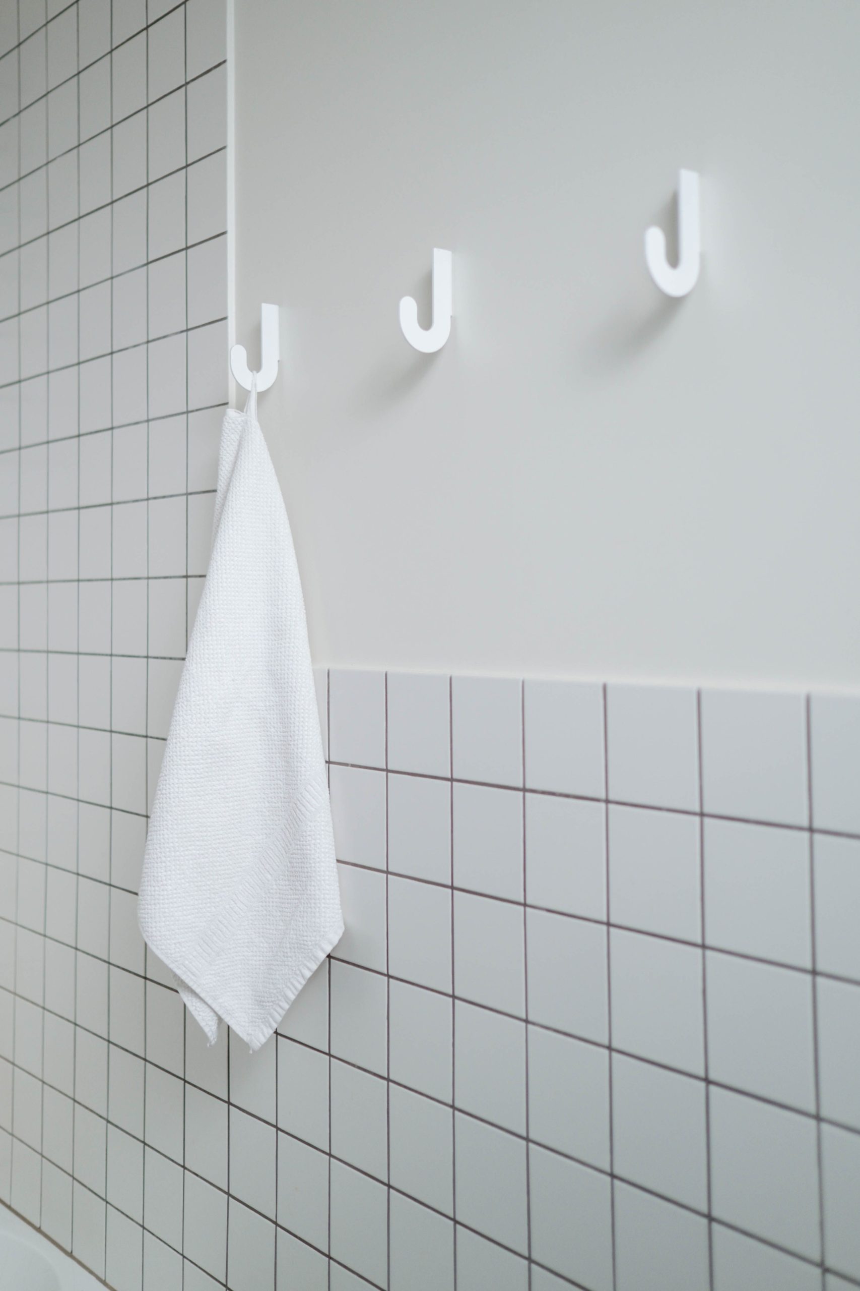 Clean minimalist bathroom with white towel hanging on hooks, emphasizing simplicity and hygiene.