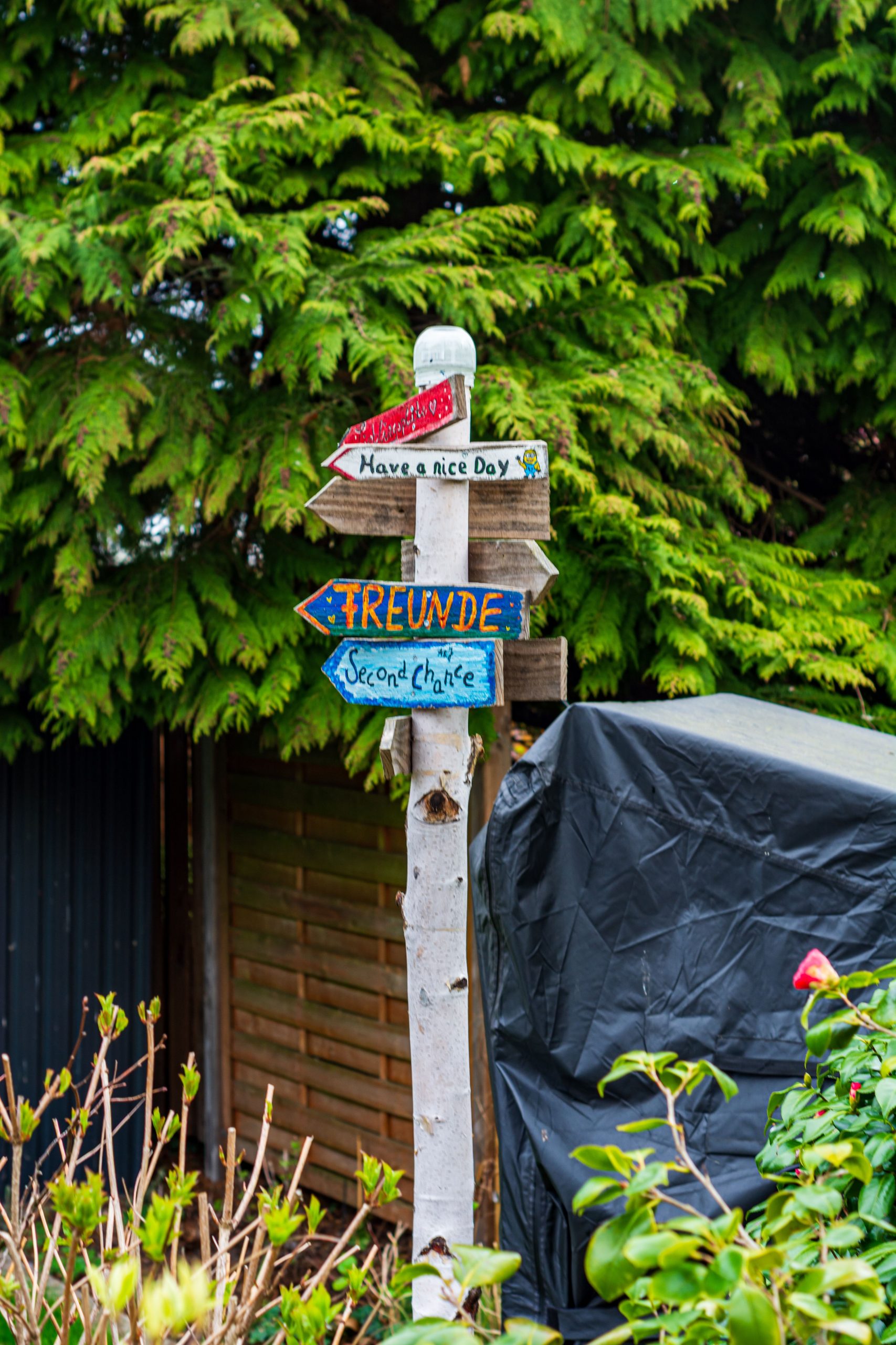 Colorful wooden signpost in a lush garden in Coesfeld, Germany. Friendly messages add charm.