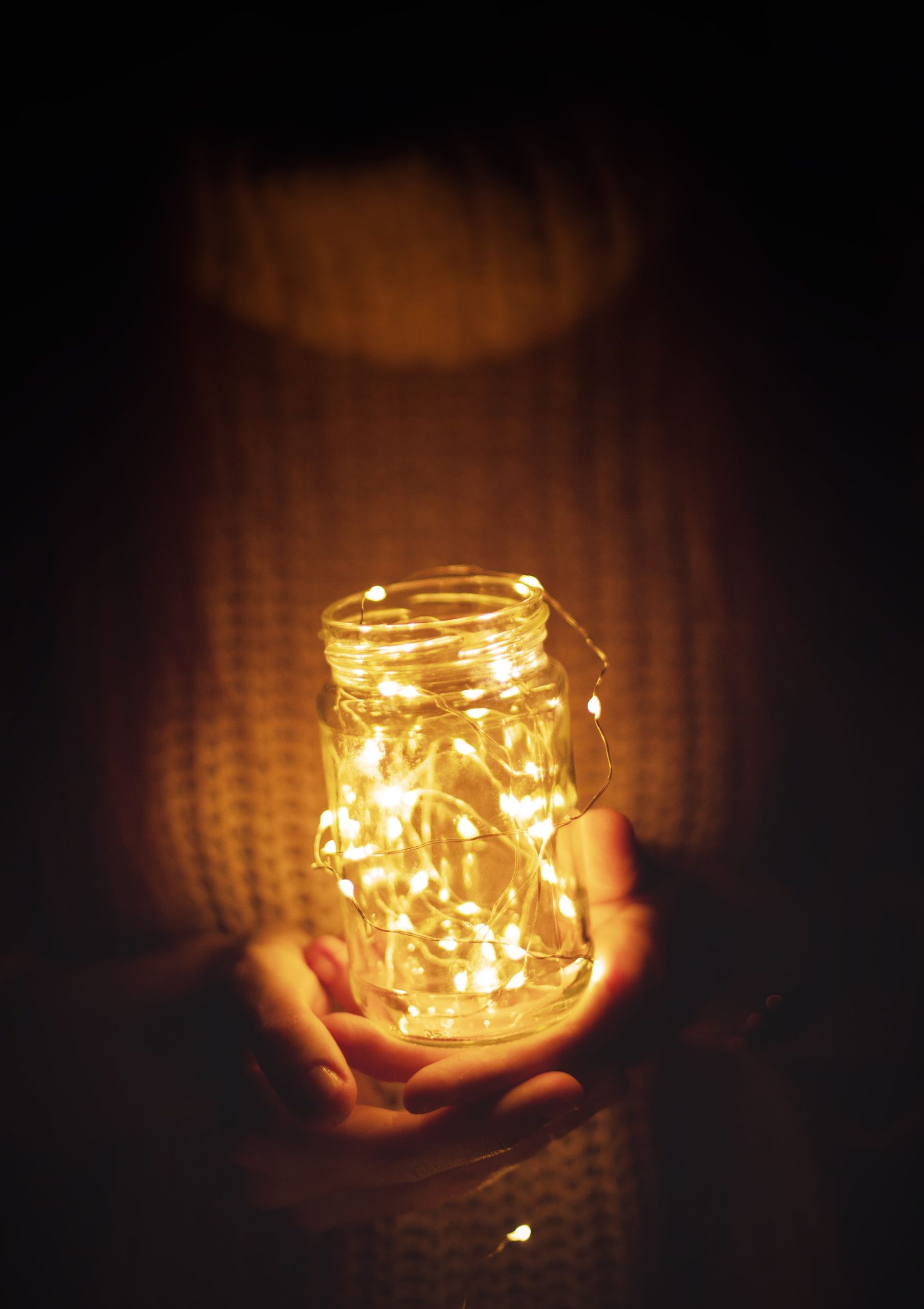 Cozy hands hold an illuminated jar of string lights, creating a warm ambient glow.