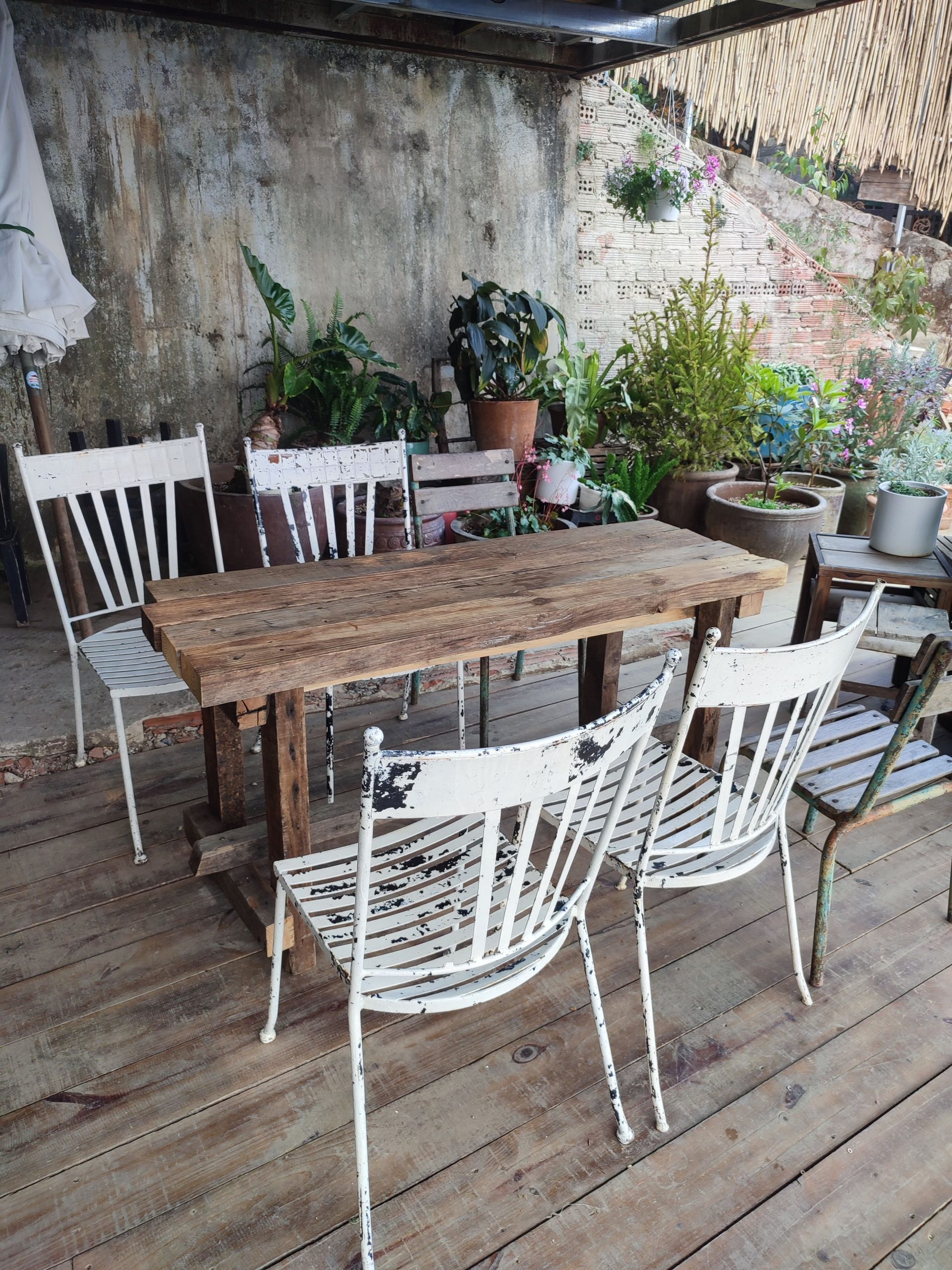 Cozy outdoor patio with rustic chairs and table surrounded by lush potted plants.