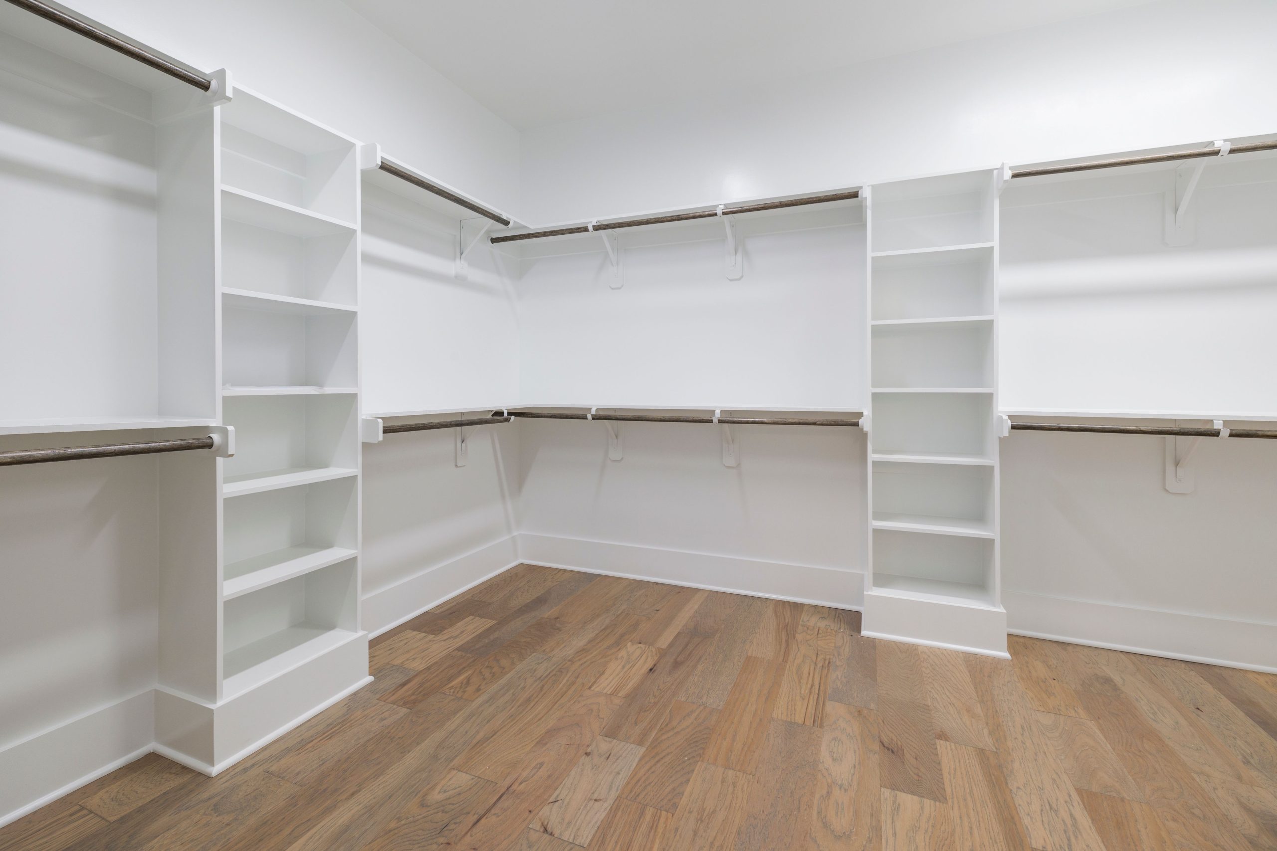 Empty modern walk-in wardrobe featuring wood floors and white shelving.