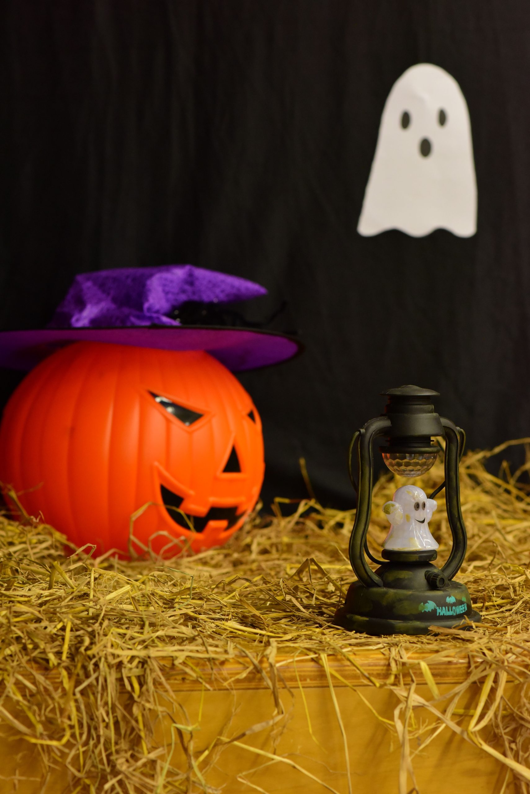 Festive Halloween scene with a pumpkin, ghost lamp, and purple witch's hat.