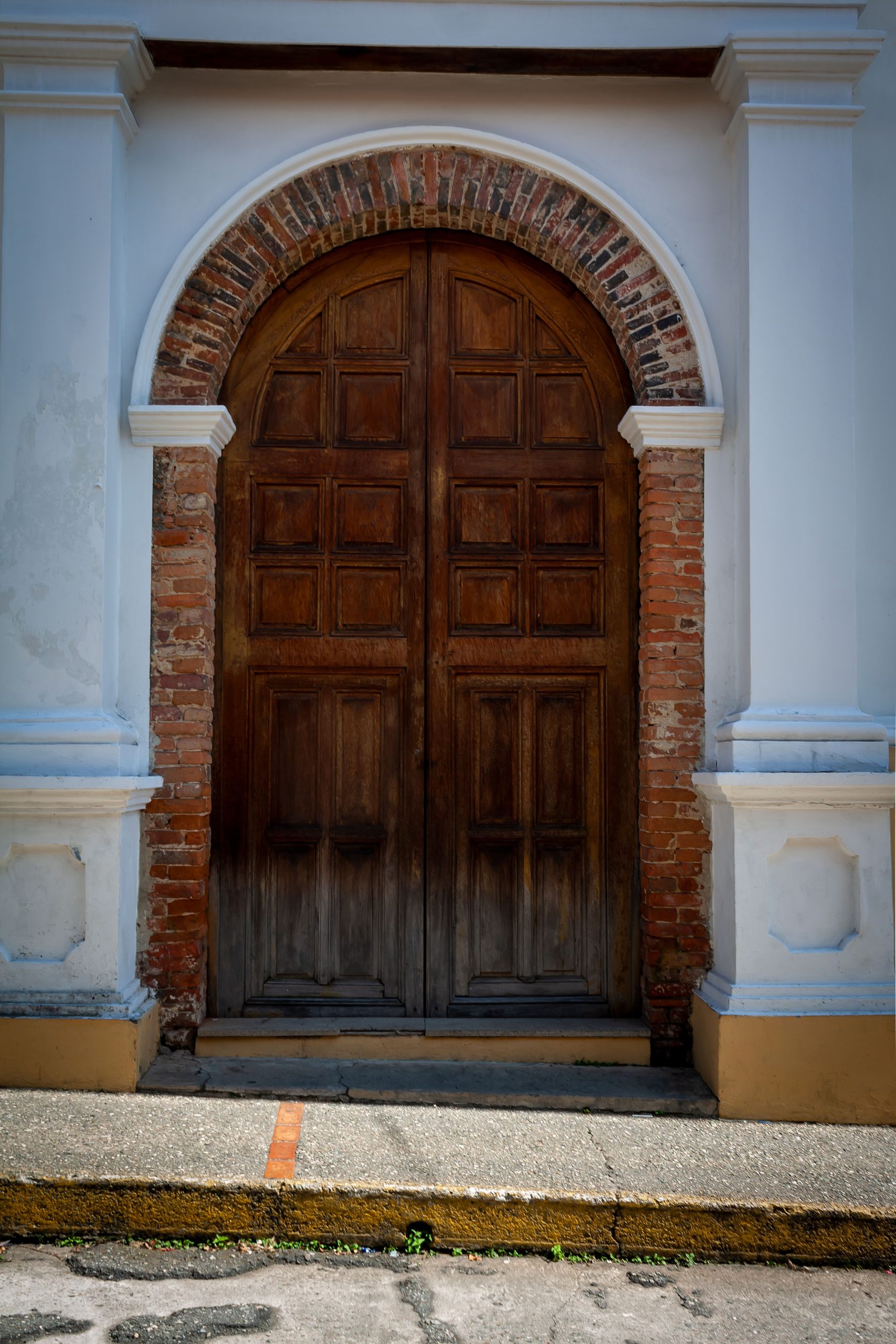 Historic arched wooden door framed by brick and plaster in Mérida, Venezuela.