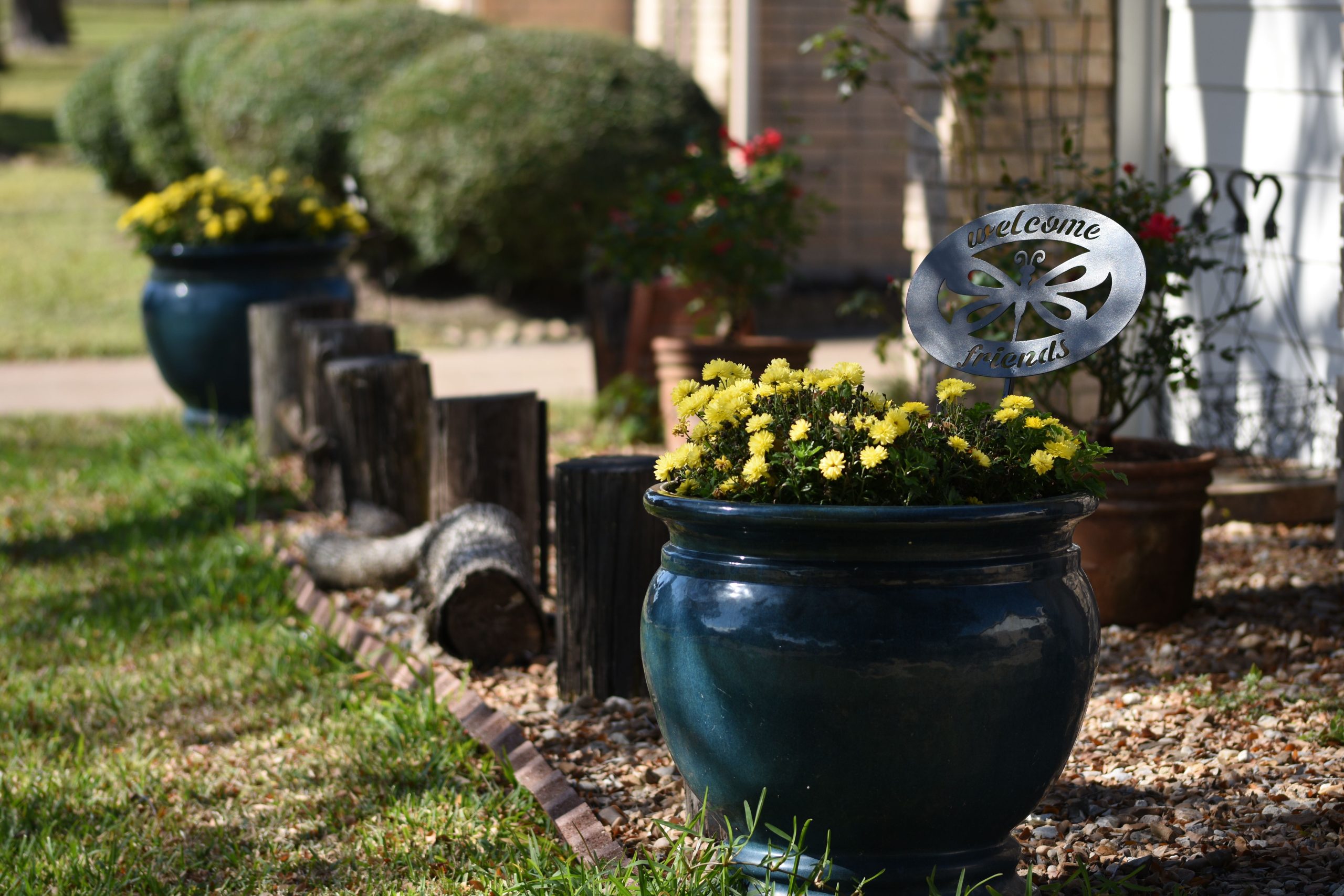 Inviting garden scene with yellow flowers in blue pots and 'Welcome Friends' sign.