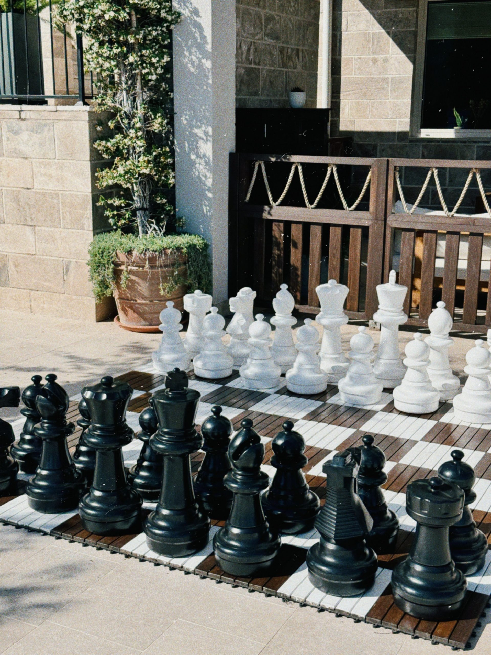Large black and white chess set outdoors on a sunny patio, perfect for strategic play.