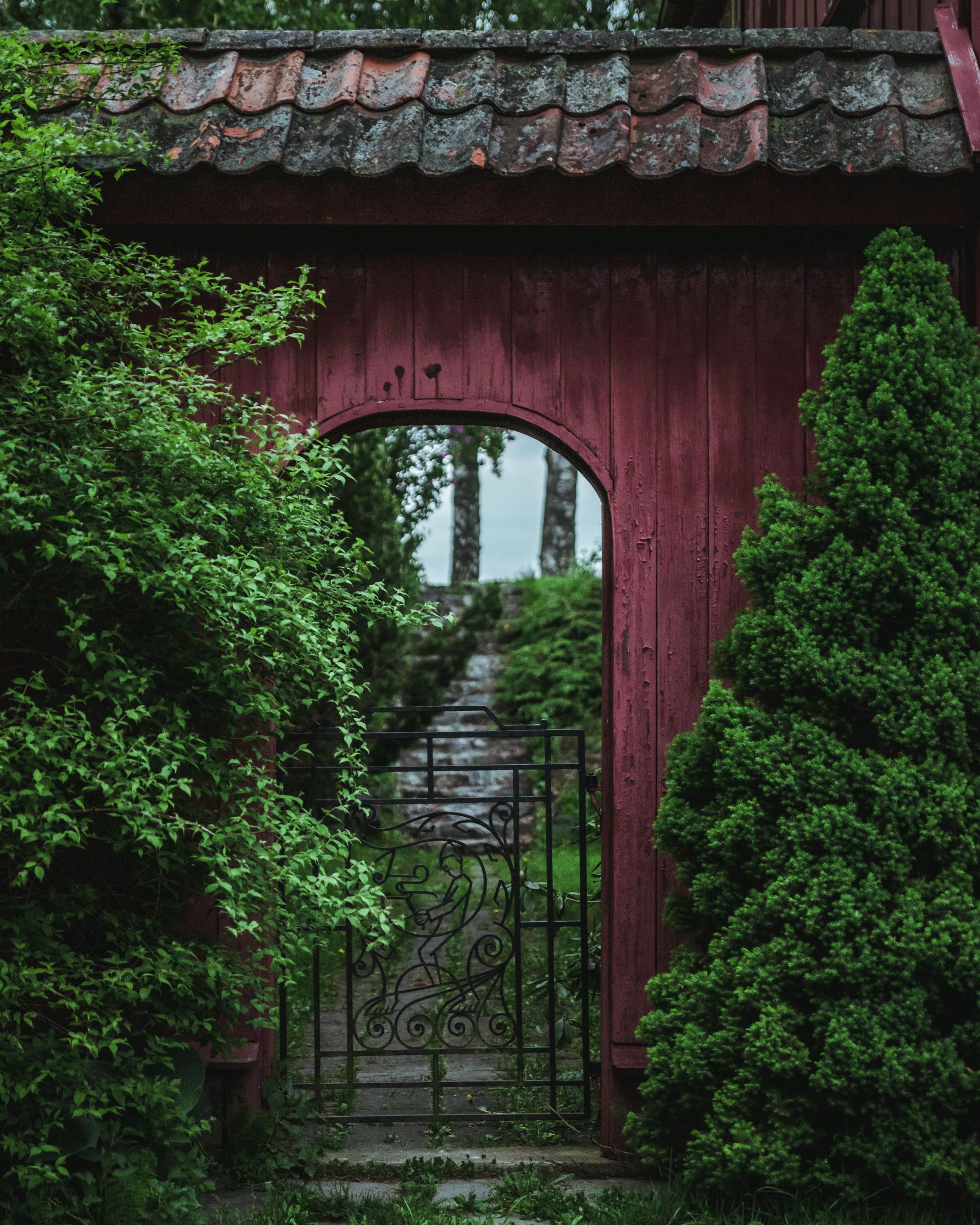 Rustic arch and gate leading to a scenic garden path in Oslo, Norway, lush greenery.