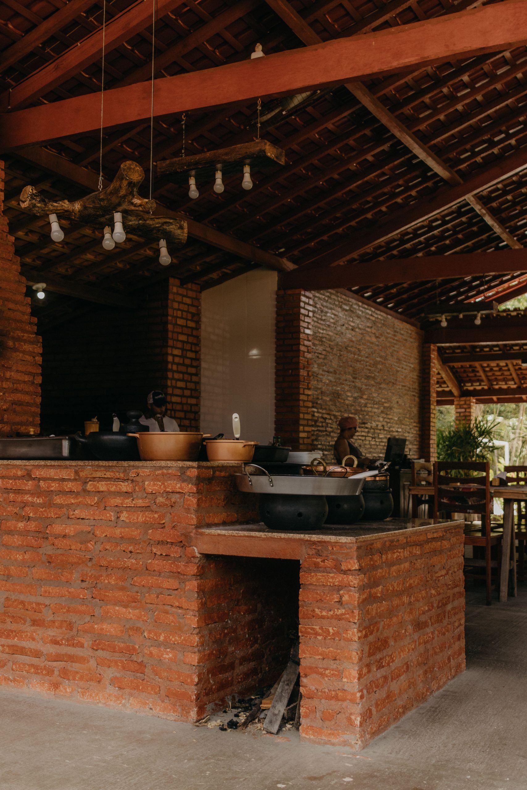 Rustic outdoor kitchen featuring a brick oven and dining area under a wooden ceiling.