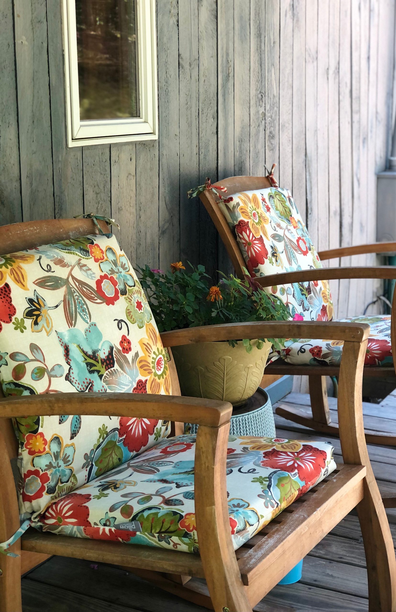 Two wooden armchairs with vibrant floral cushions on a cozy porch setting. Ideal for relaxing moments.