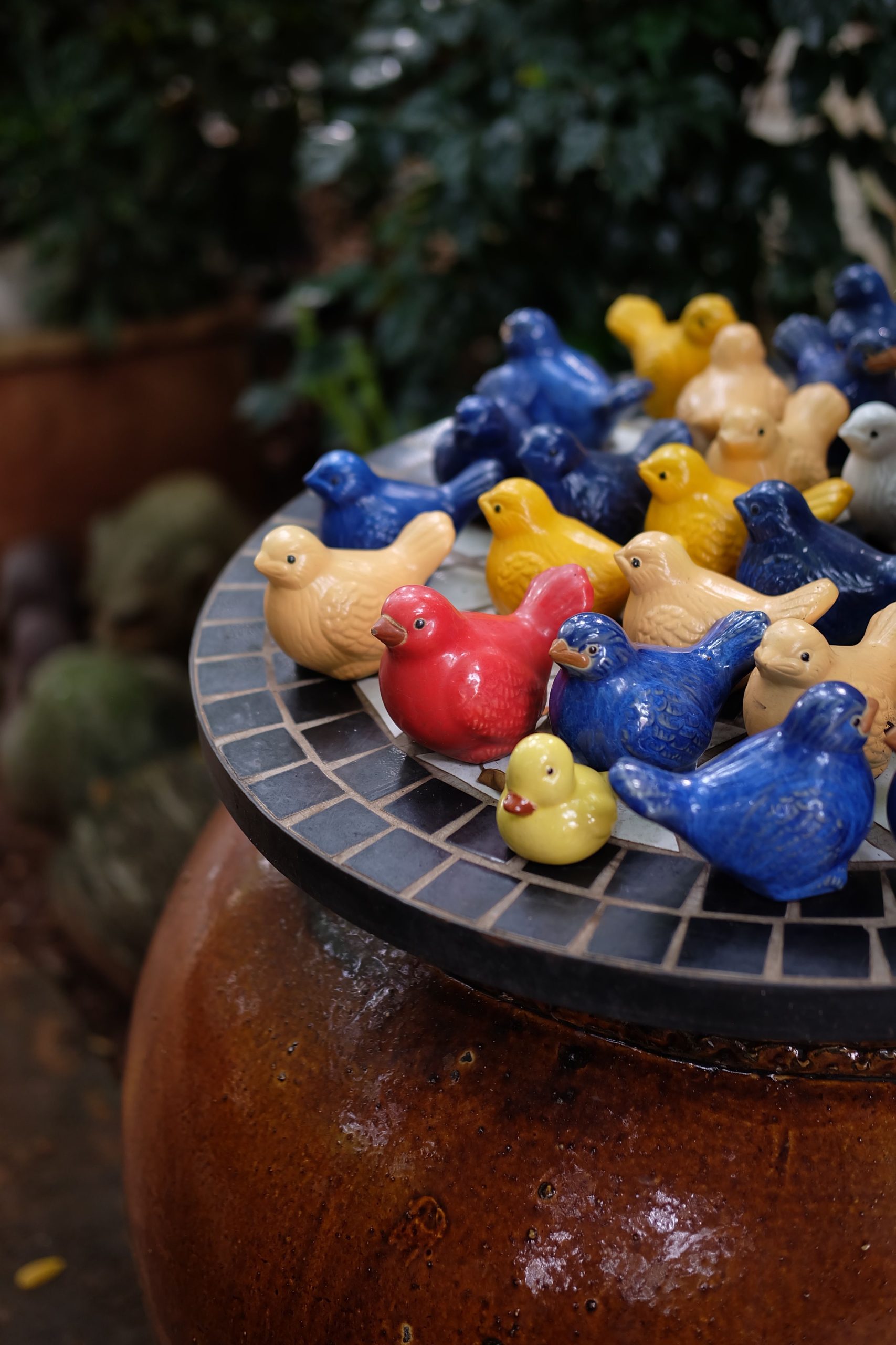 Vibrant ceramic bird statues in various colors on a tiled surface outdoors.