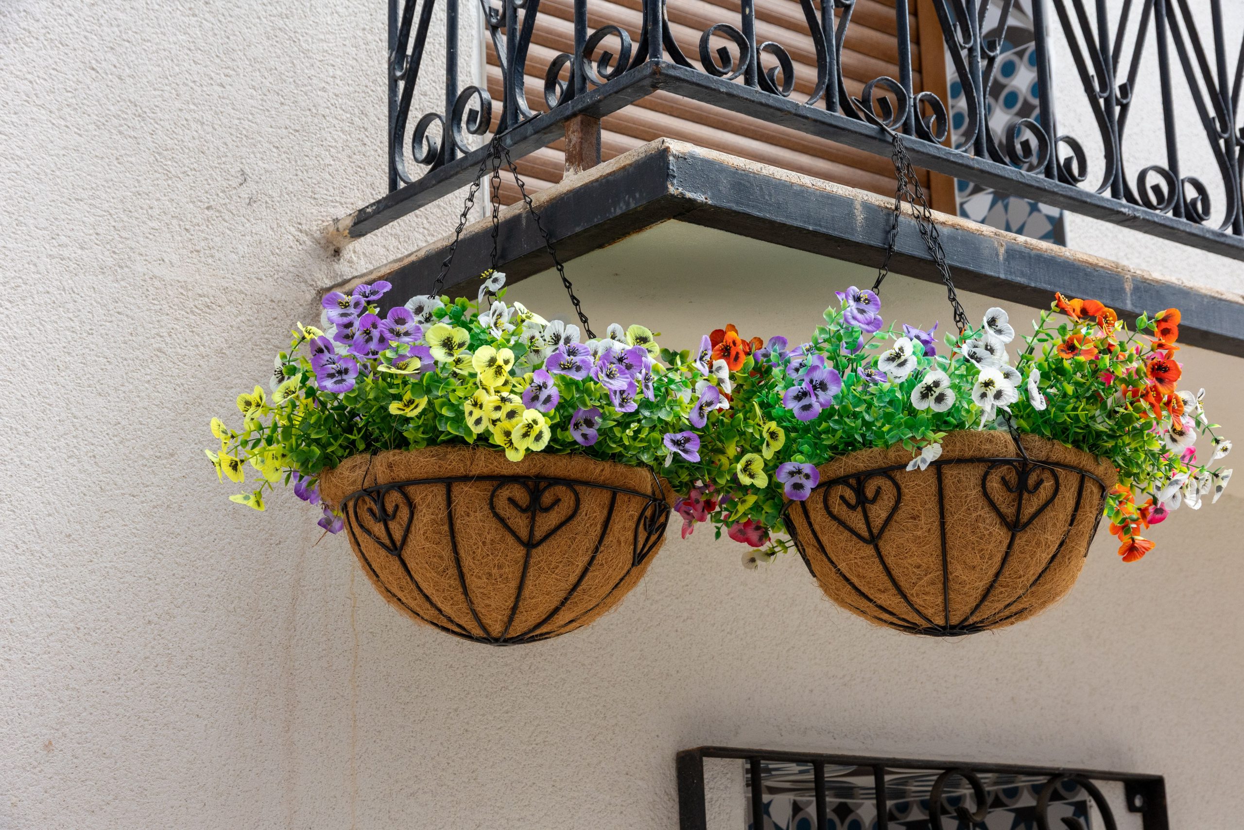 Vibrant hanging floral baskets decorate a quaint balcony on a sunny day.