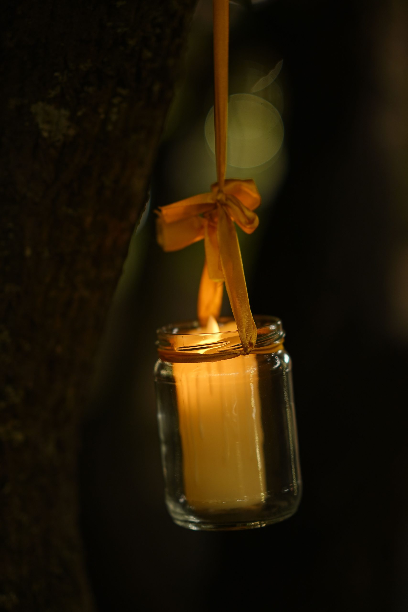 Warm glowing candle in a glass jar hanging from a tree branch, creating a cozy ambiance.