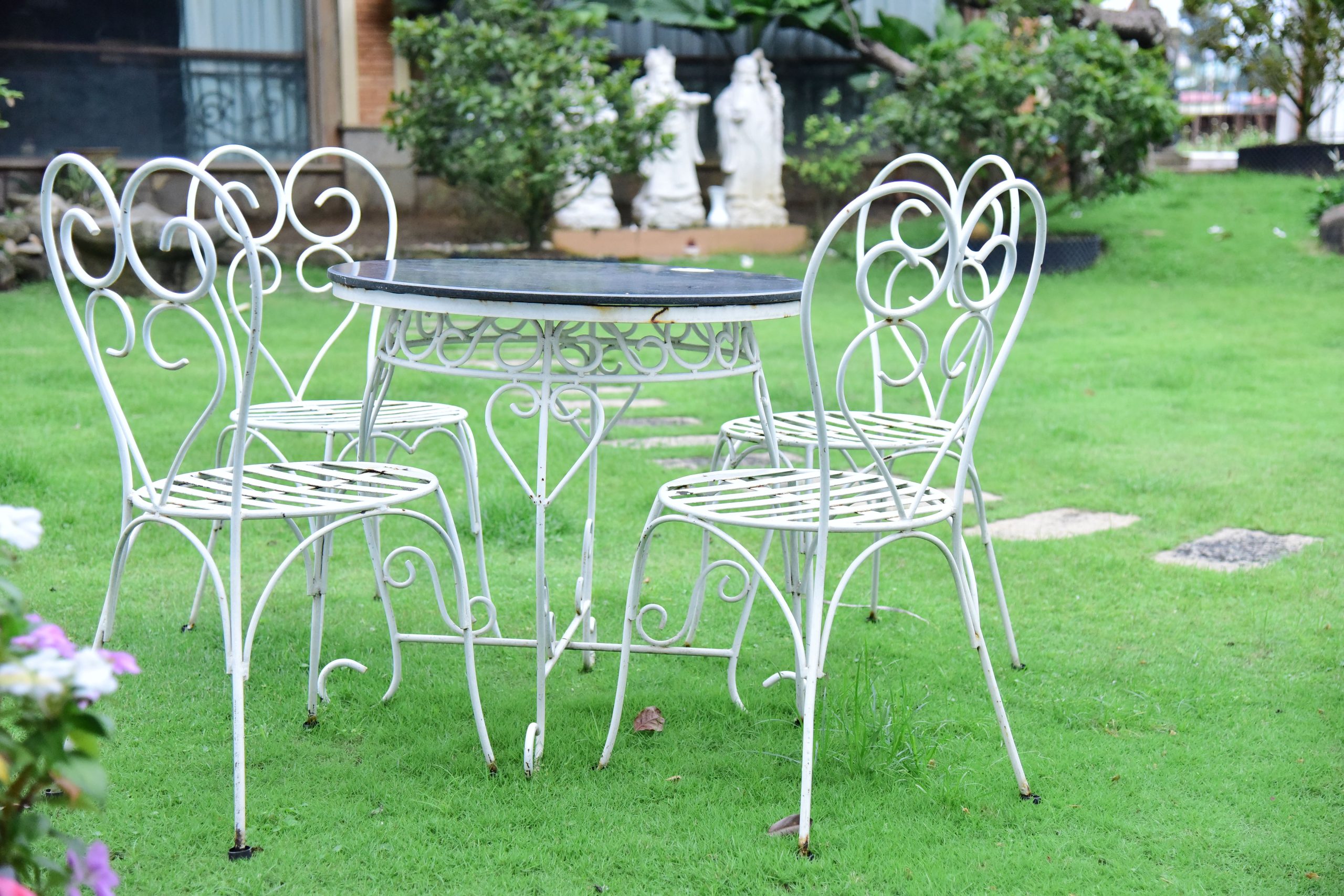 White iron table and chairs set on a vibrant green lawn outdoors.