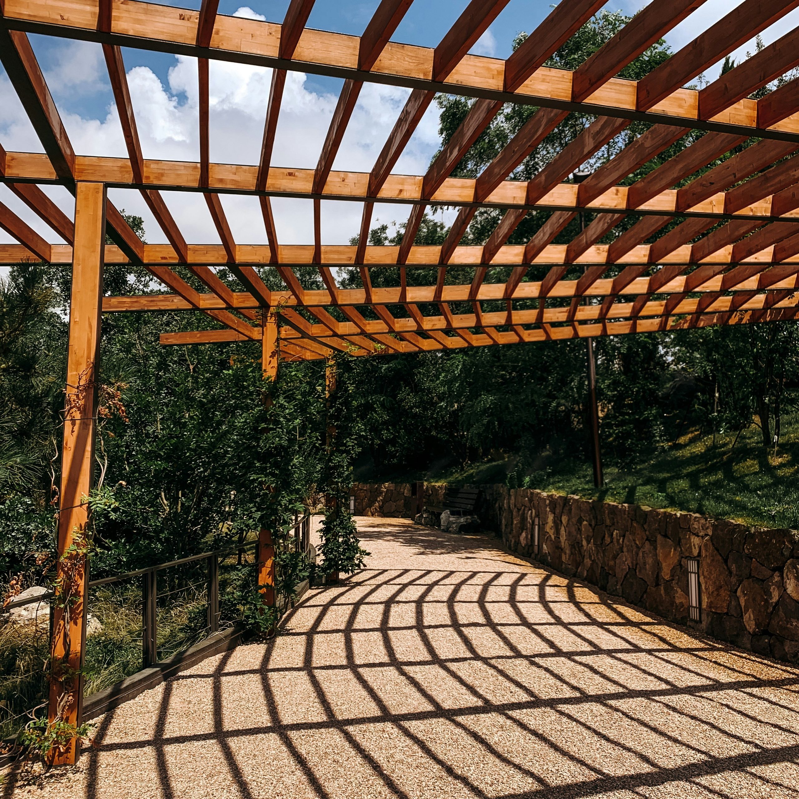 Wooden pergola casting shadows on a gravel path.