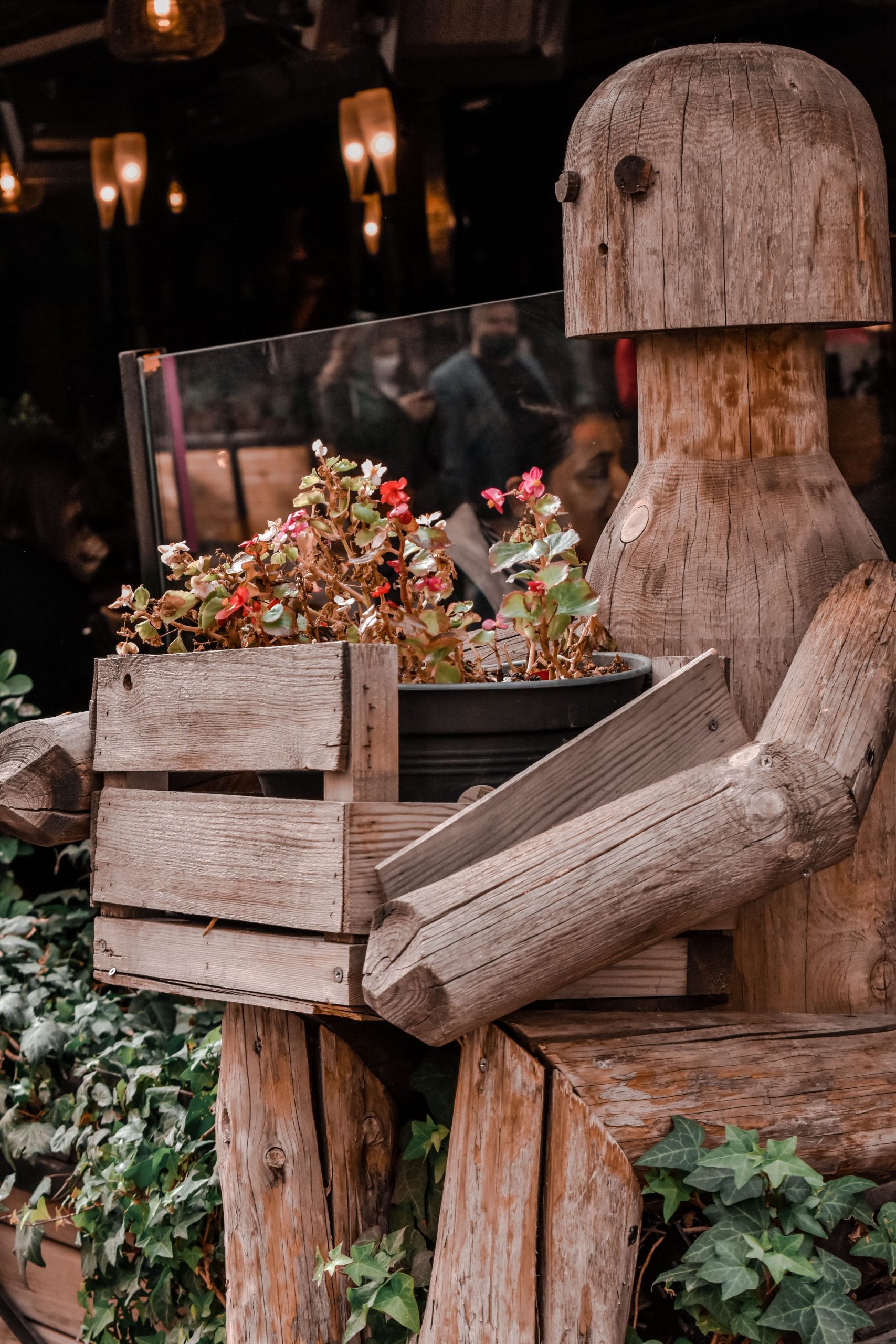 Wooden sculpture holding a box of autumn flowers outdoors, creating a rustic decor scene.