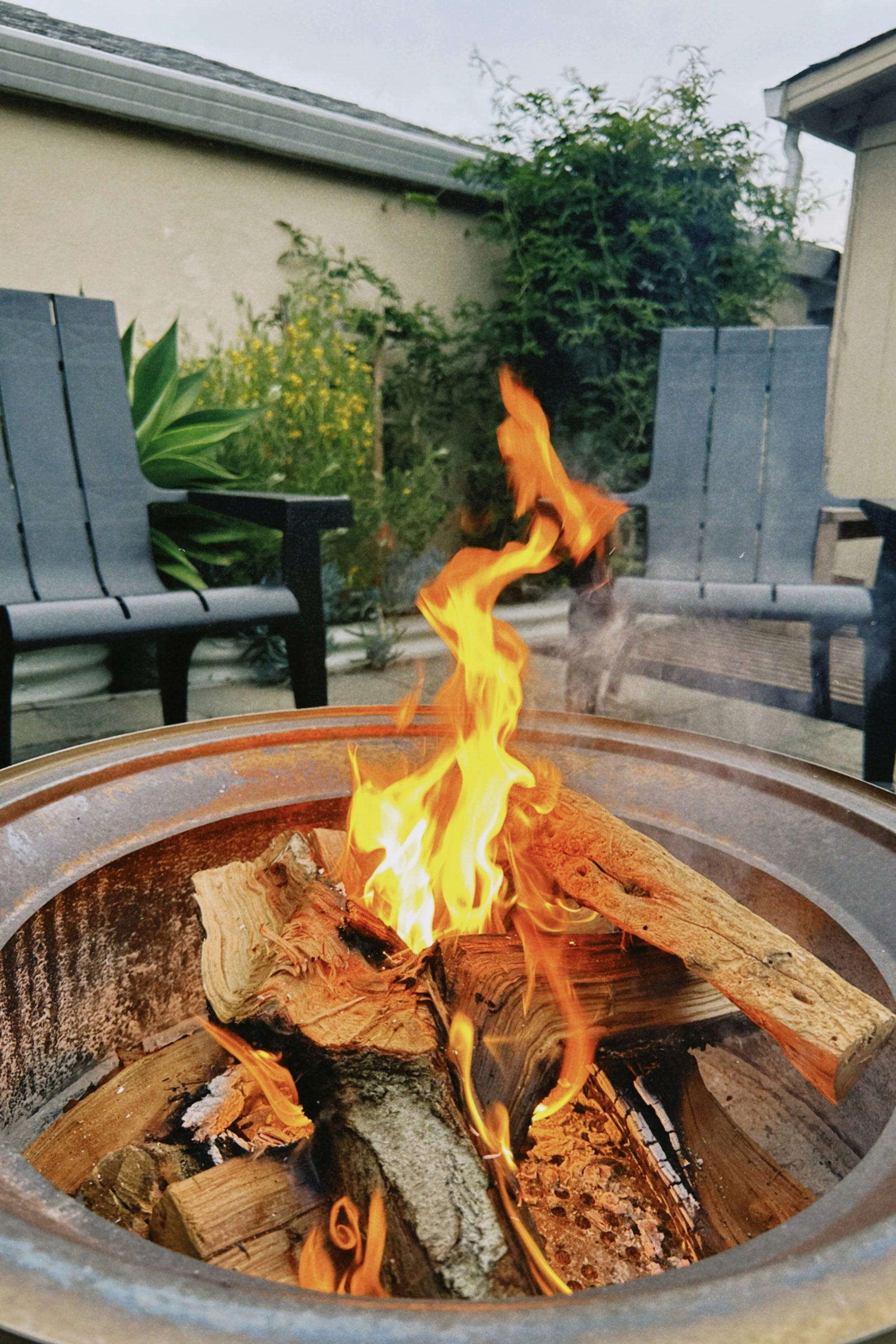 A backyard fire pit with burning logs and two chairs.