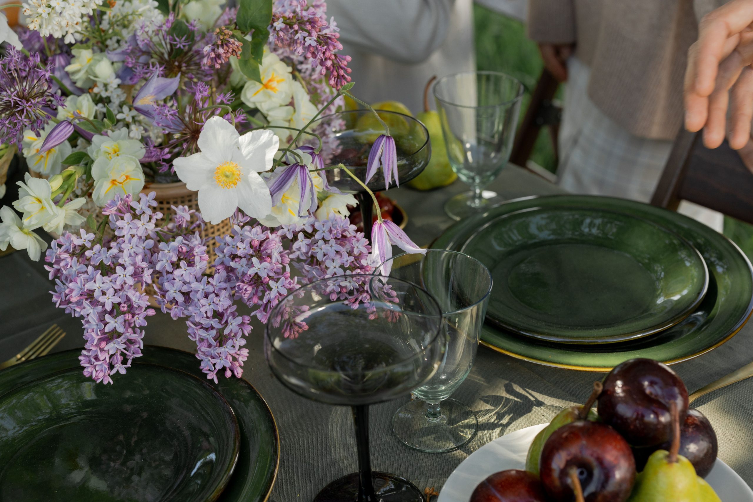 A beautifully arranged outdoor table with flowers, fruits, and green plates.