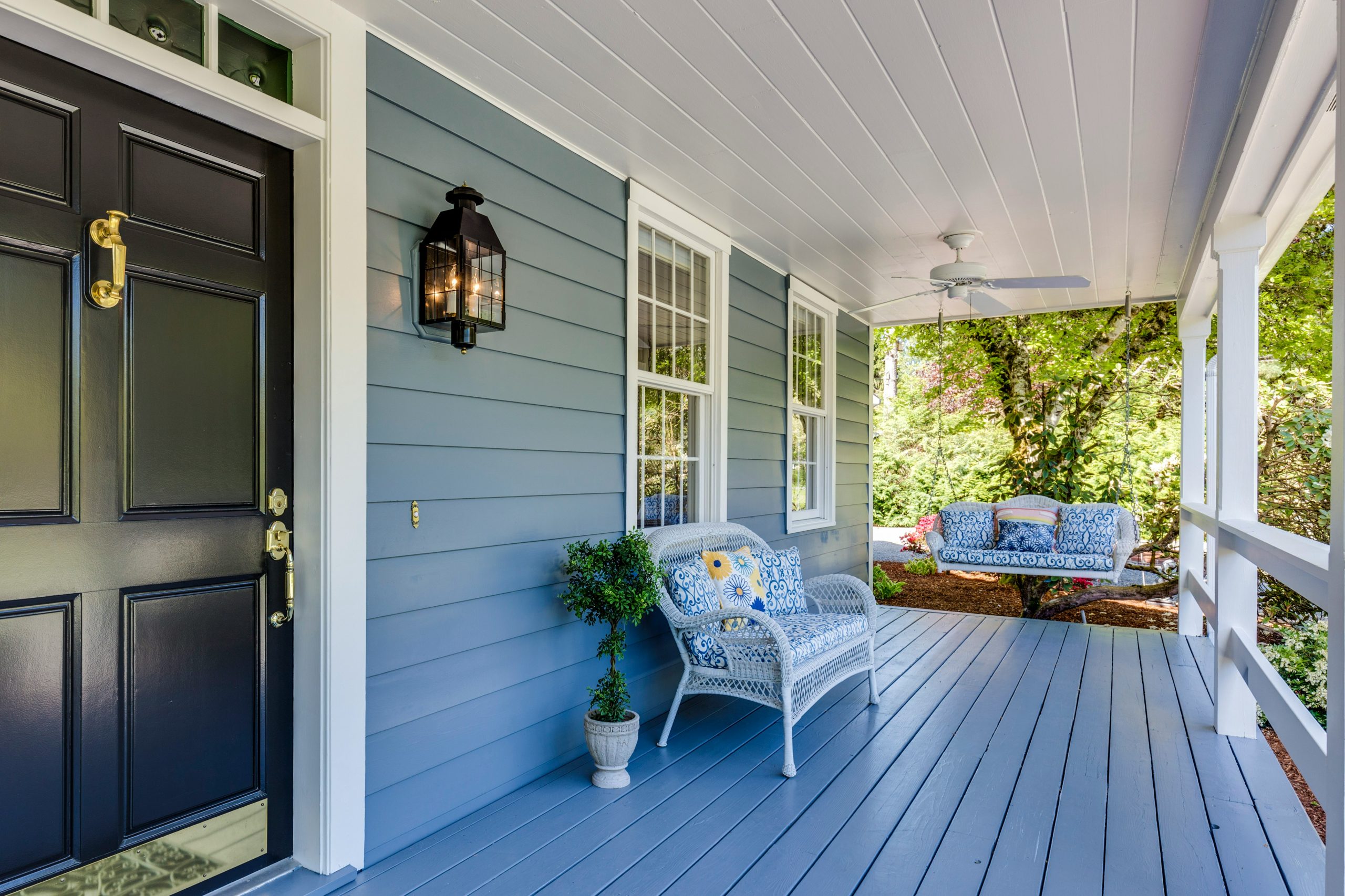 A blue porch with a black door, white wicker furniture, and a hanging swing