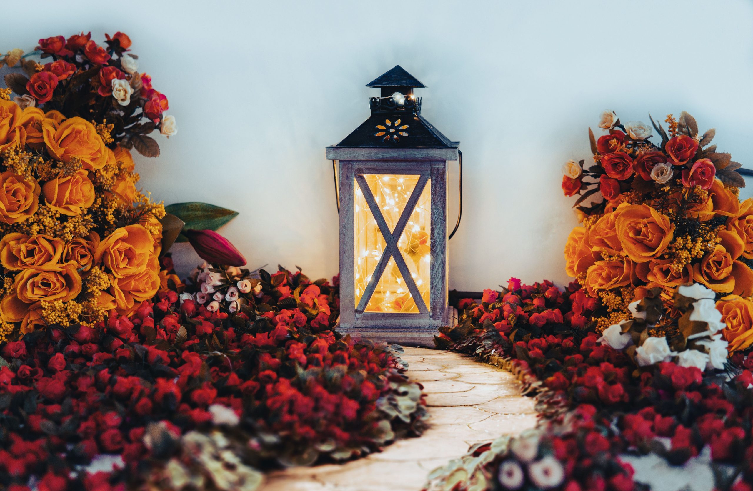 A charming lantern surrounded by bright orange and red floral arrangements, evoking a warm autumnal ambiance.