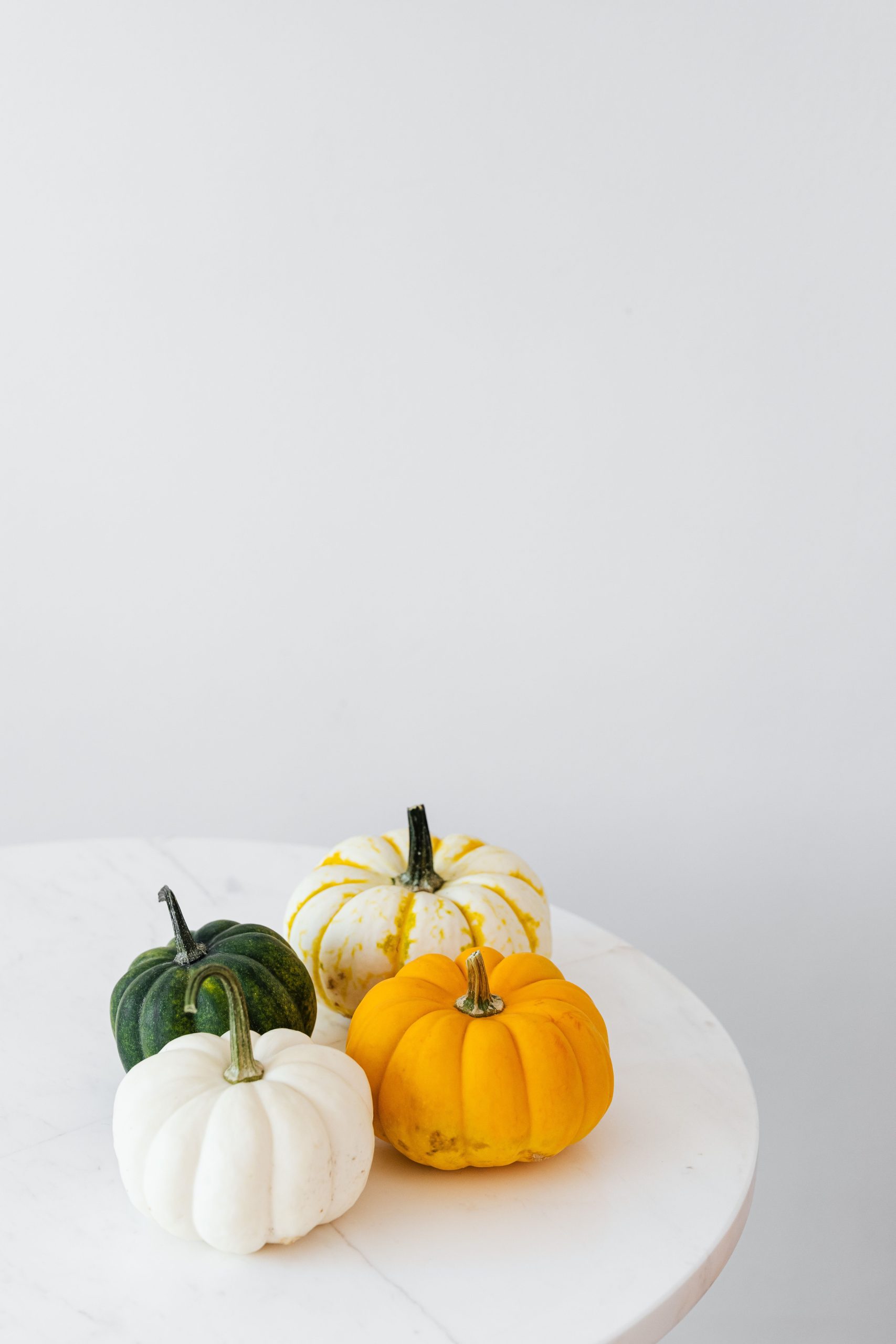 A collection of vibrant pumpkins on a marble table with a minimalist gray background.