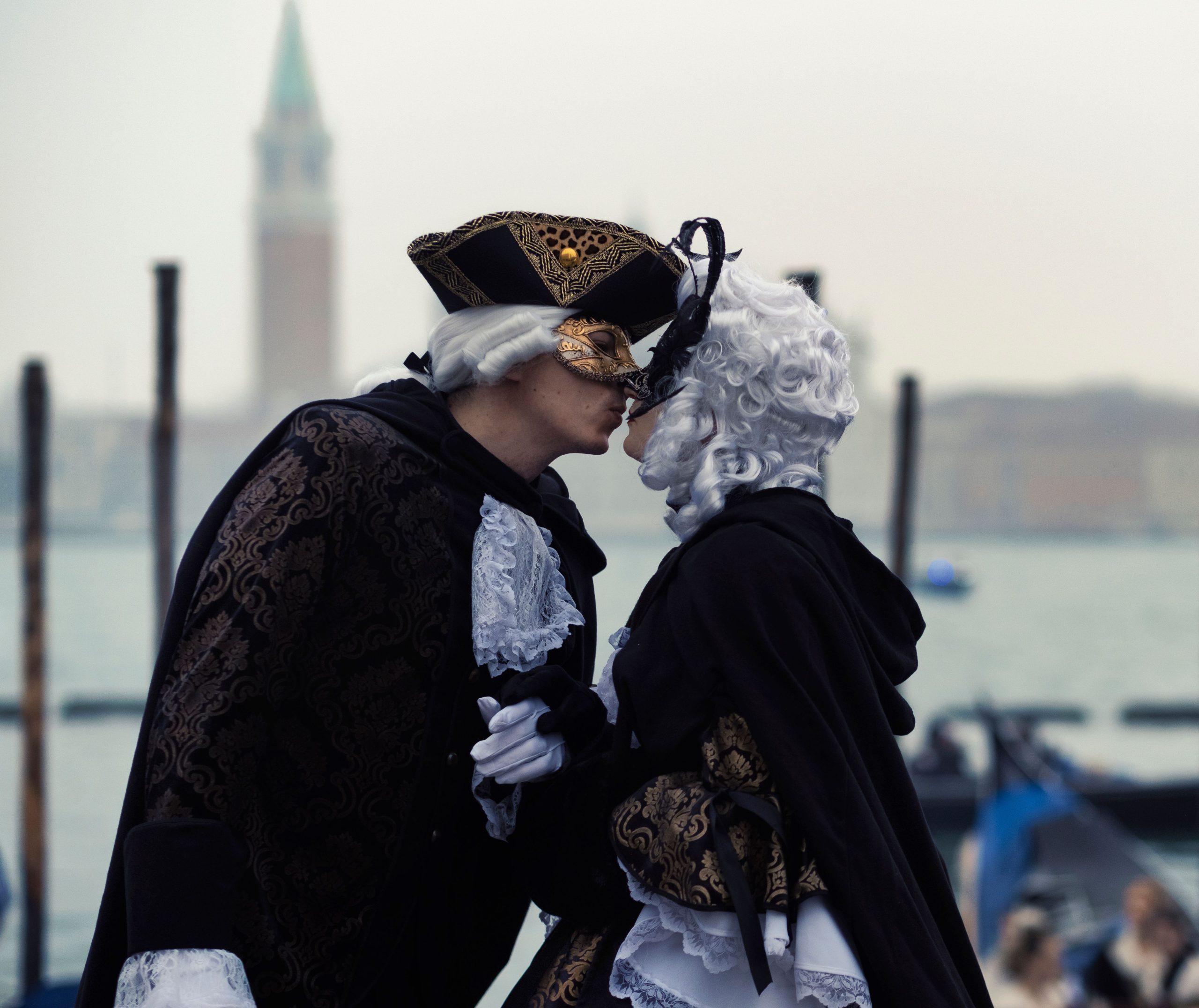 A couple in elaborate costumes and masks share a tender moment in Venice.