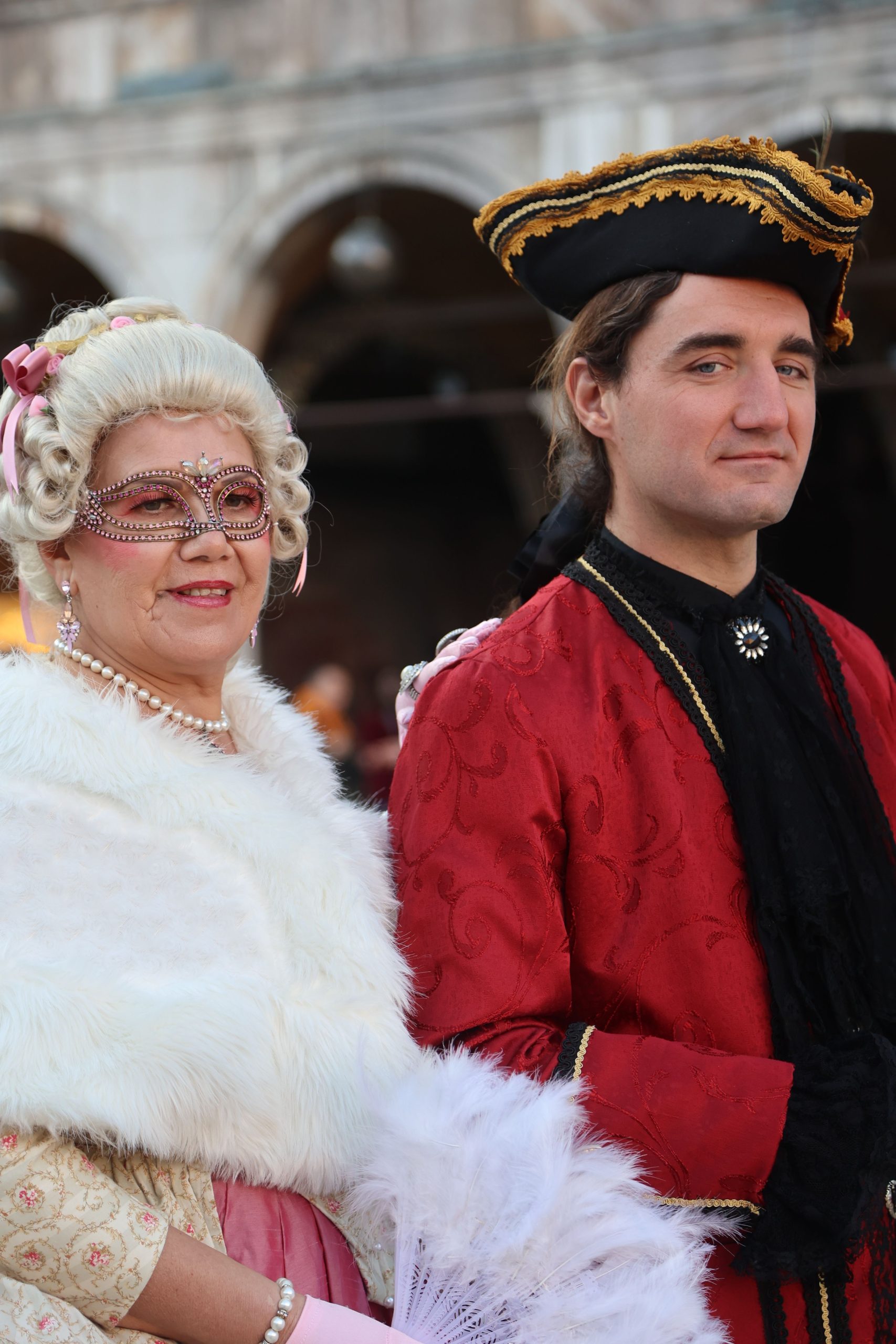 A couple in ornate masquerade costumes at a festive outdoor event, showcasing historical elegance.