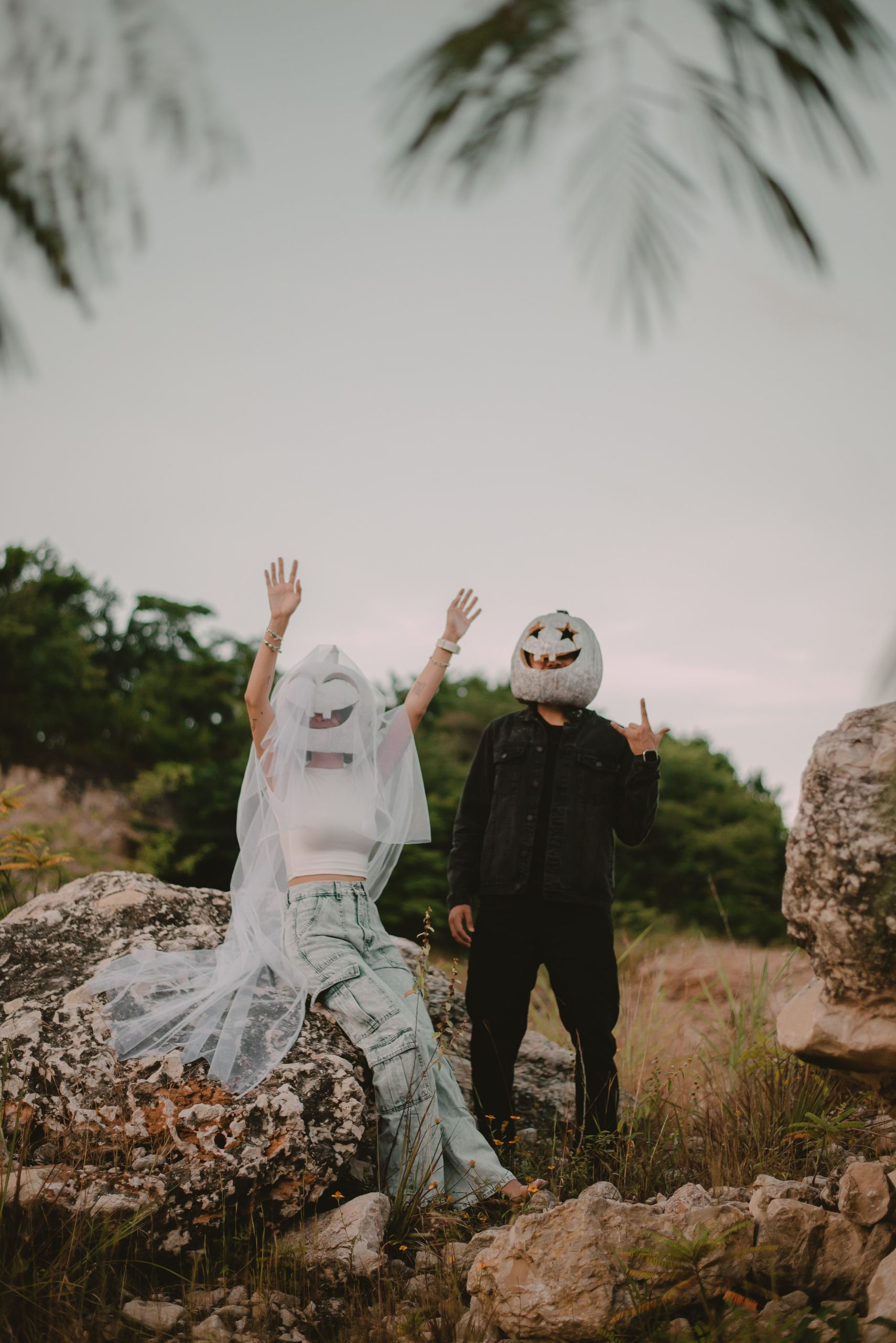 A couple wearing pumpkin masks posing in a rural setting, embracing Halloween spirit.