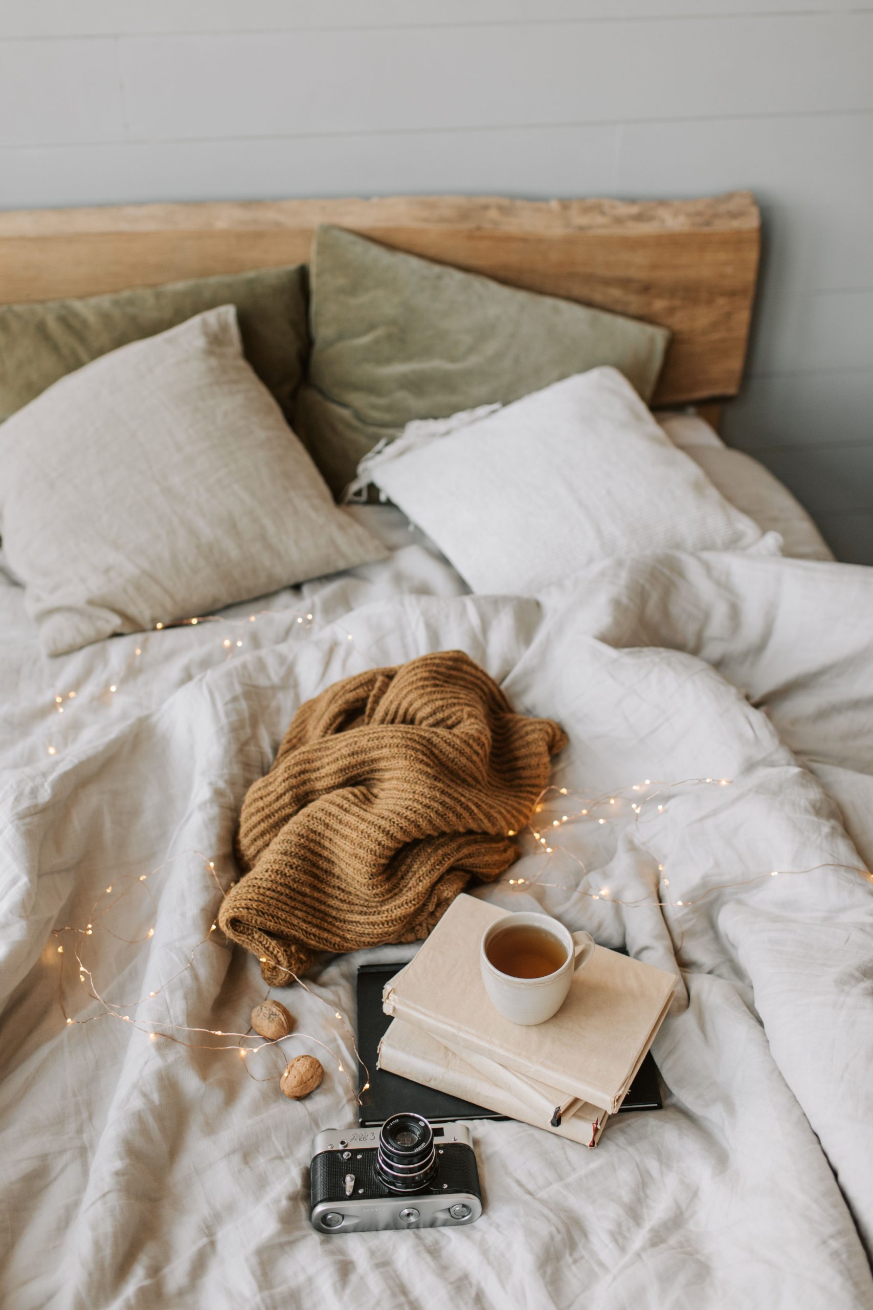 A cozy autumn bed setup with a hot drink, camera, and books, creating a vintage vibe.