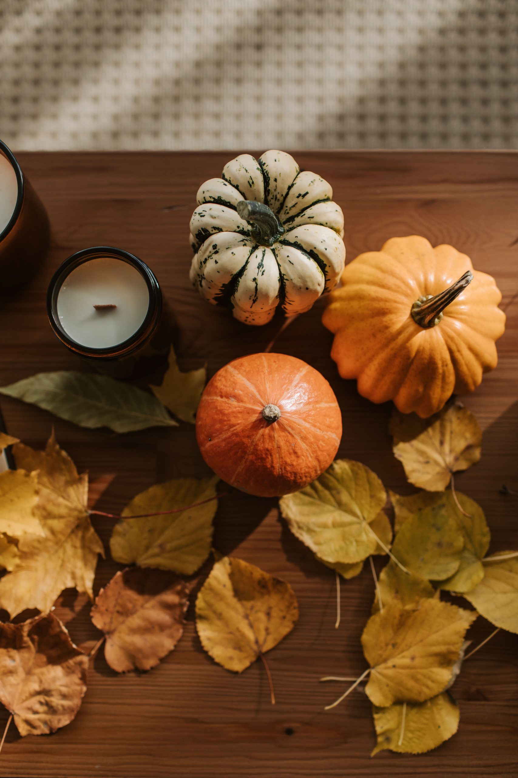 A cozy autumn flat lay featuring pumpkins, candles, and dried leaves on a wooden surface.