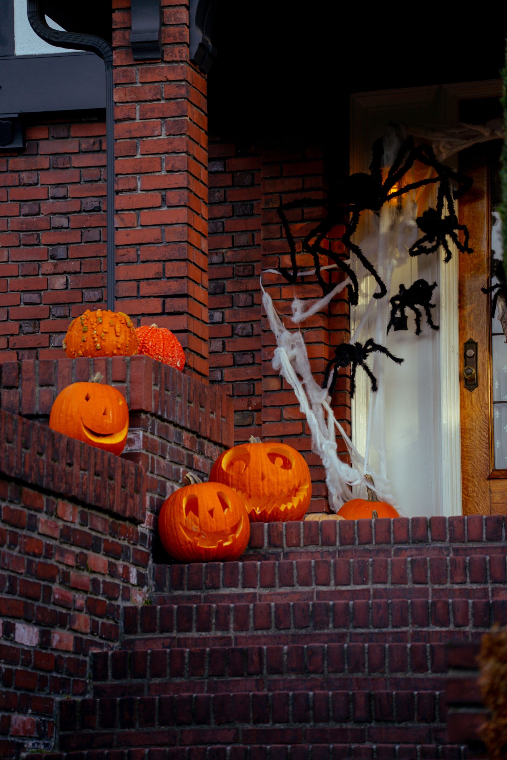 A cozy entrance decorated with pumpkins and spider webs for Halloween on a brick porch.
