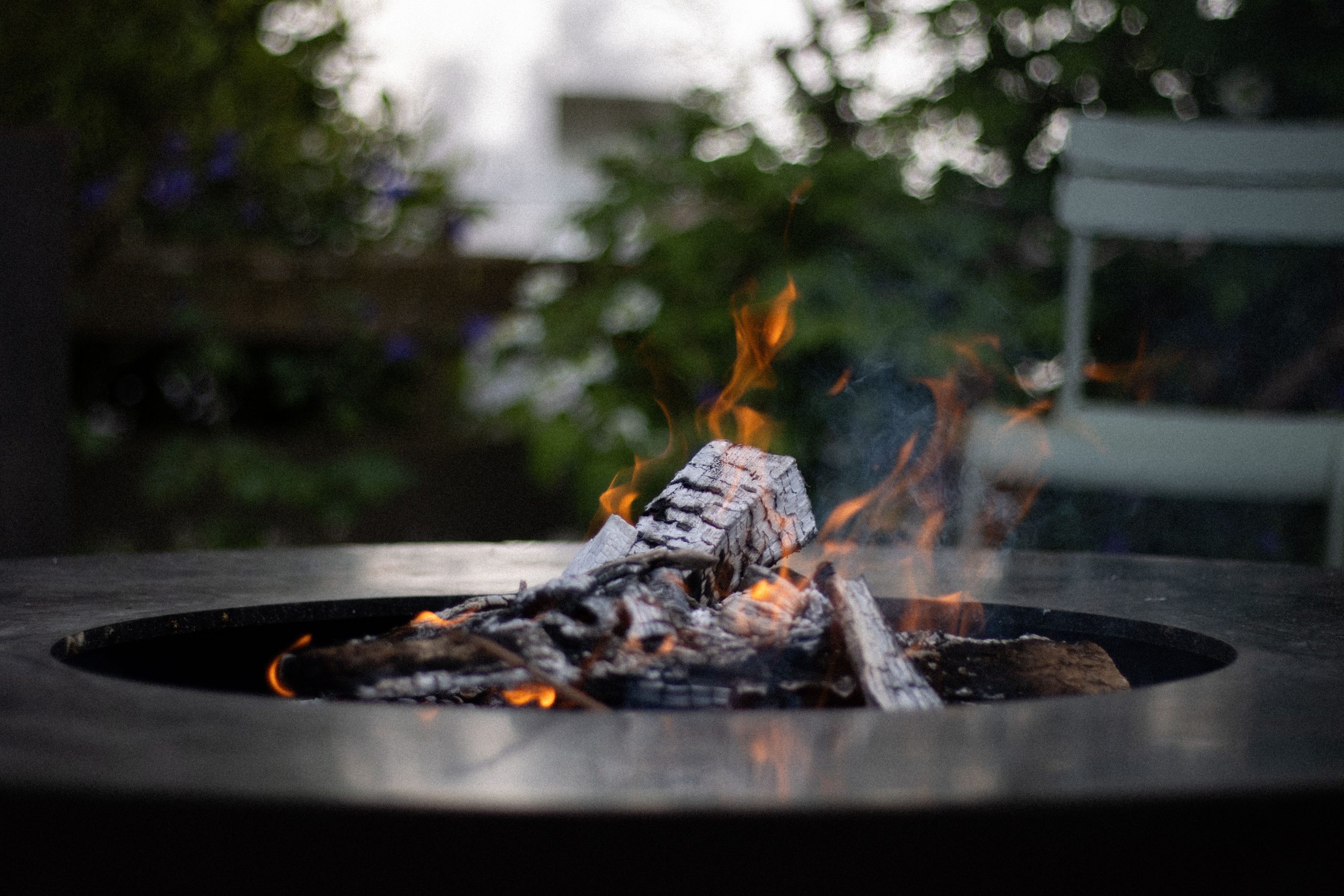 A cozy fire pit with burning logs in a serene garden, perfect for outdoor relaxation.