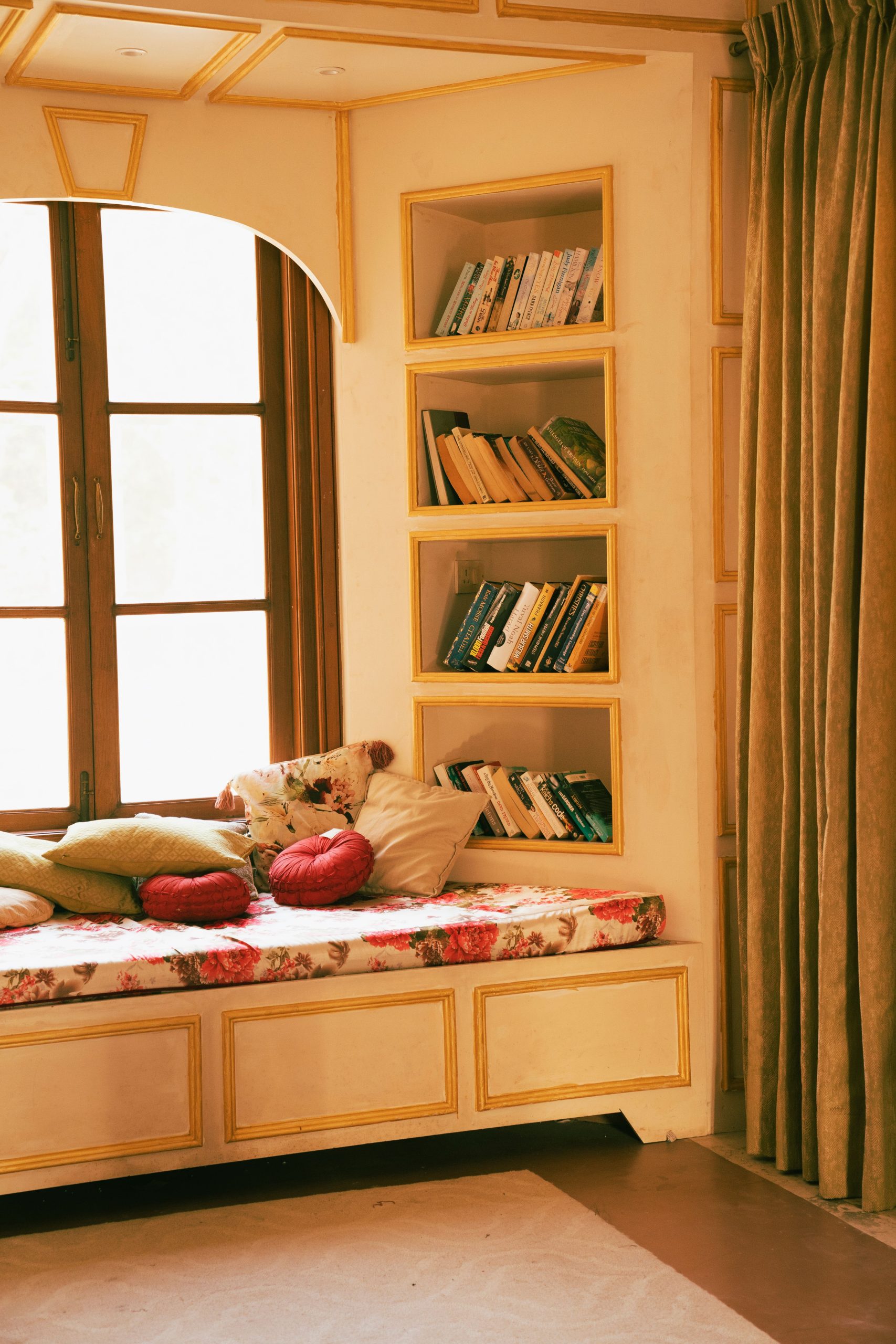 A cozy reading nook with a cushioned window seat, pillows, and built-in bookshelves in a home interior.