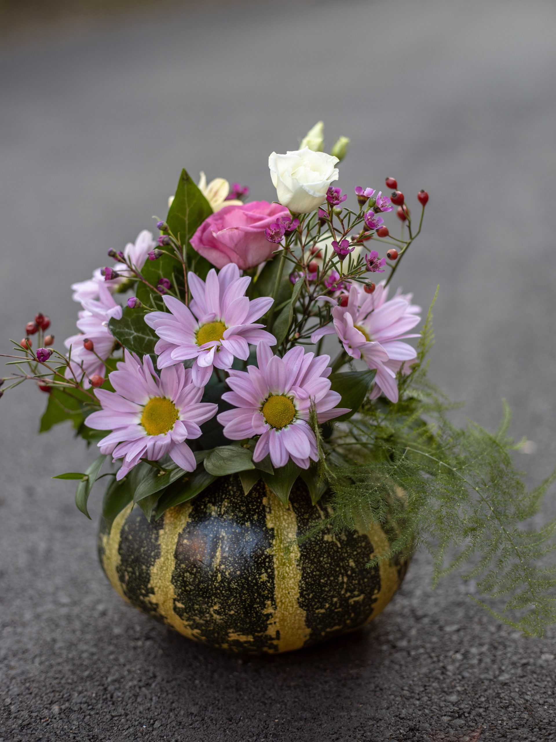 A creative floral arrangement in a pumpkin vase with daisies and roses.
