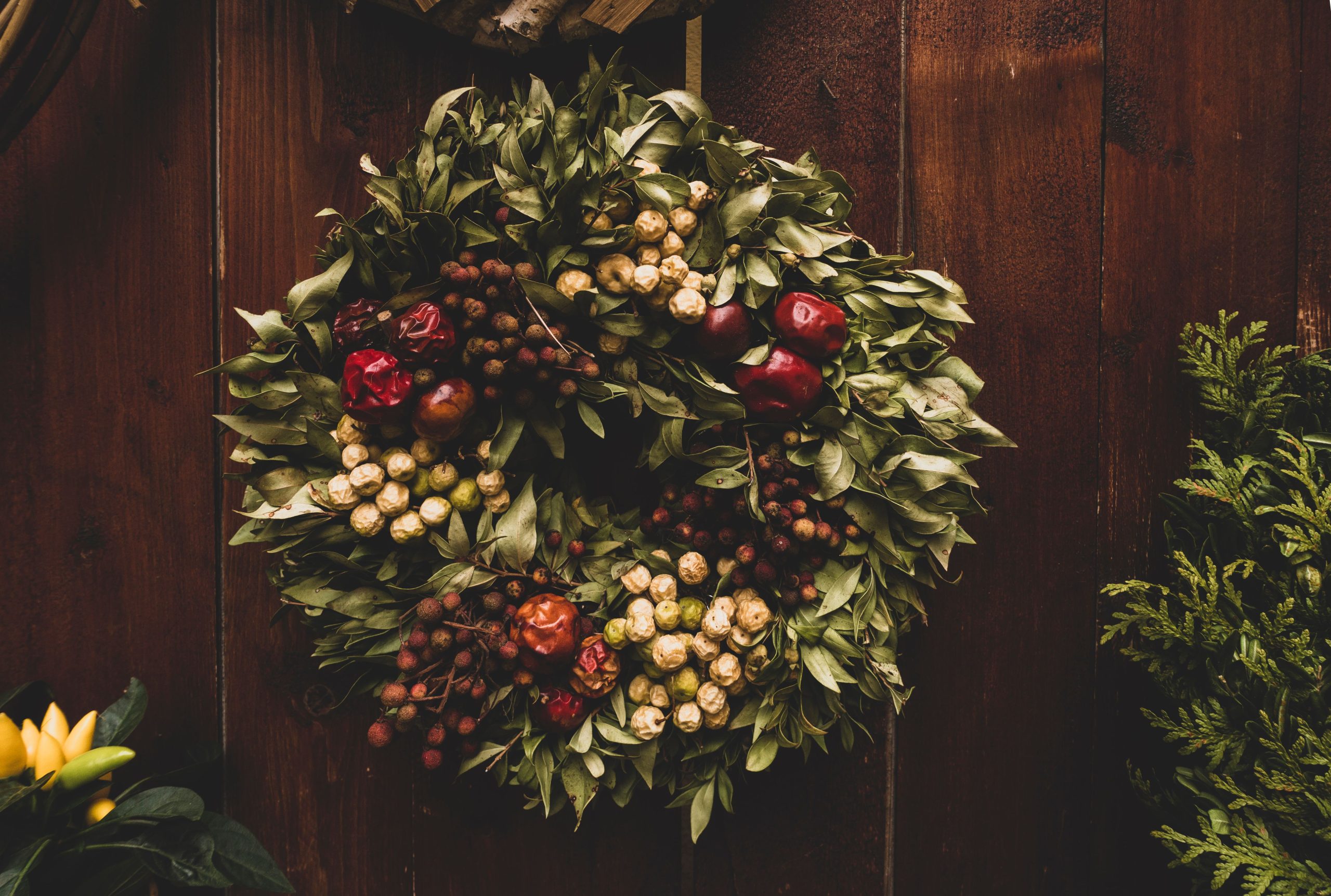 A decorative green and red wreath with berries hanging on a rustic wooden door.