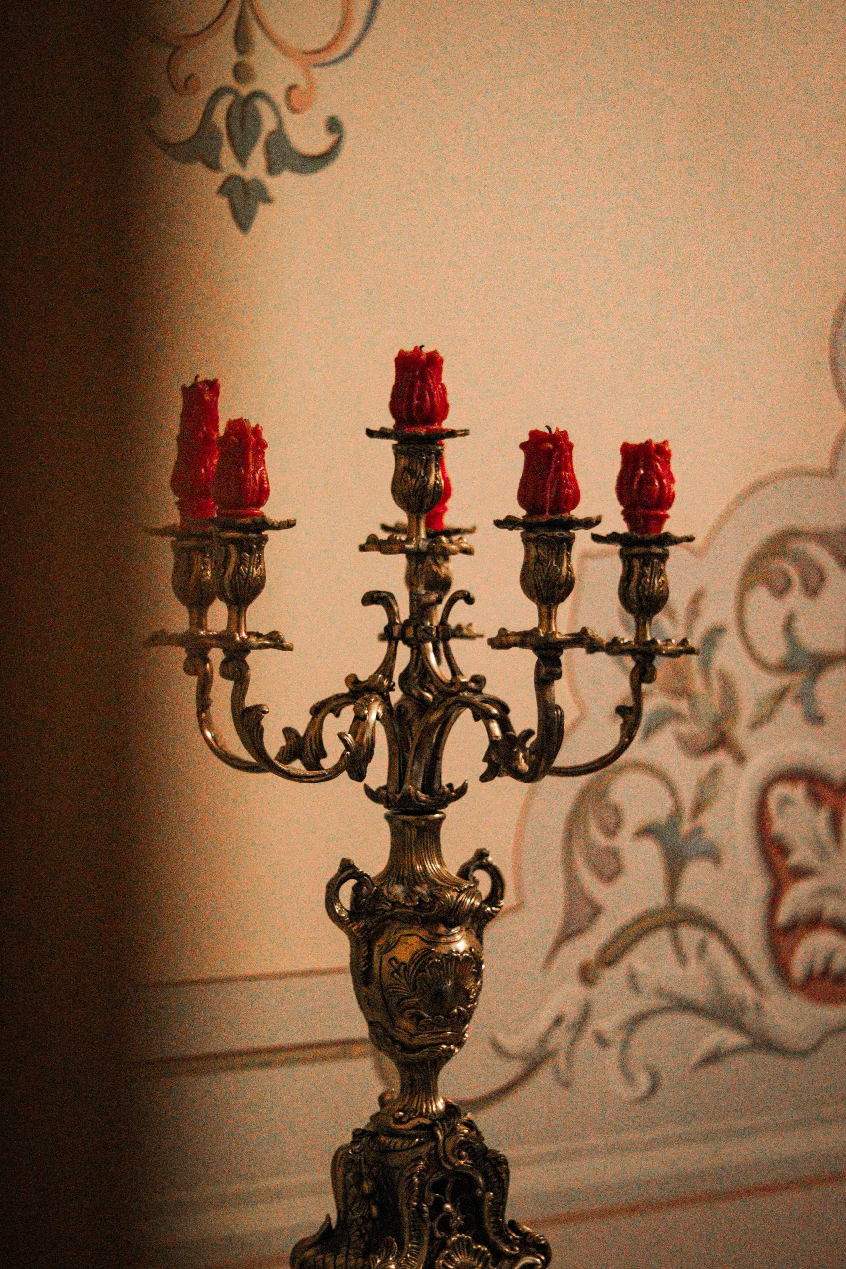 A decorative vintage candelabra with red candles, set against ornate wall patterns.