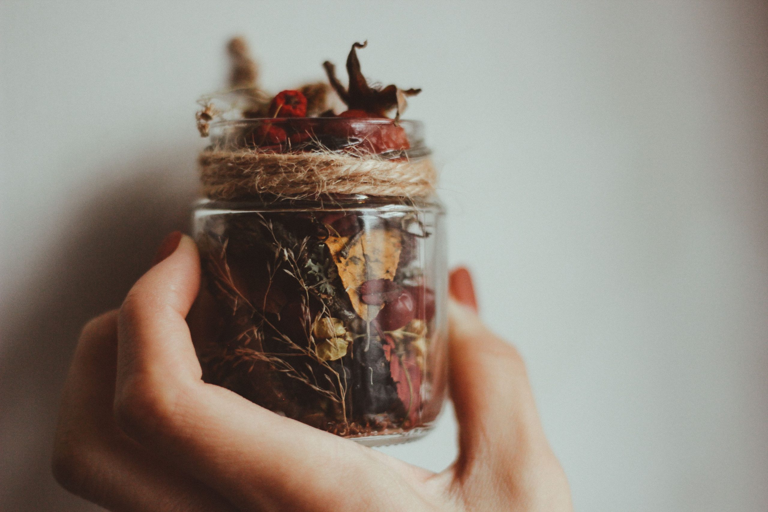 A hand holding a decorative jar filled with dried flowers and leaves, wrapped with twine.