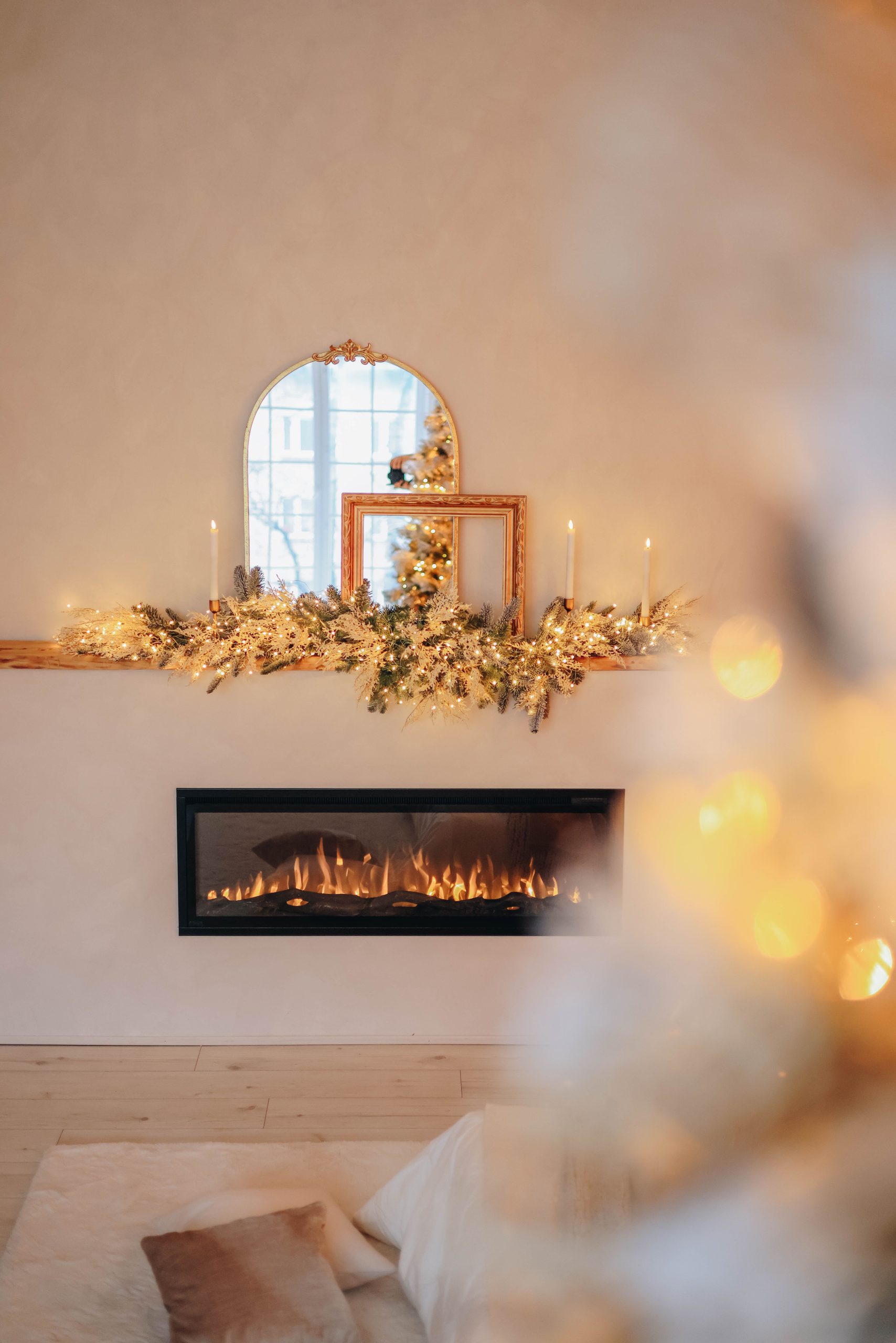 A modern interior featuring a cozy fireplace decorated with festive Christmas garlands and a stylish mirror above.