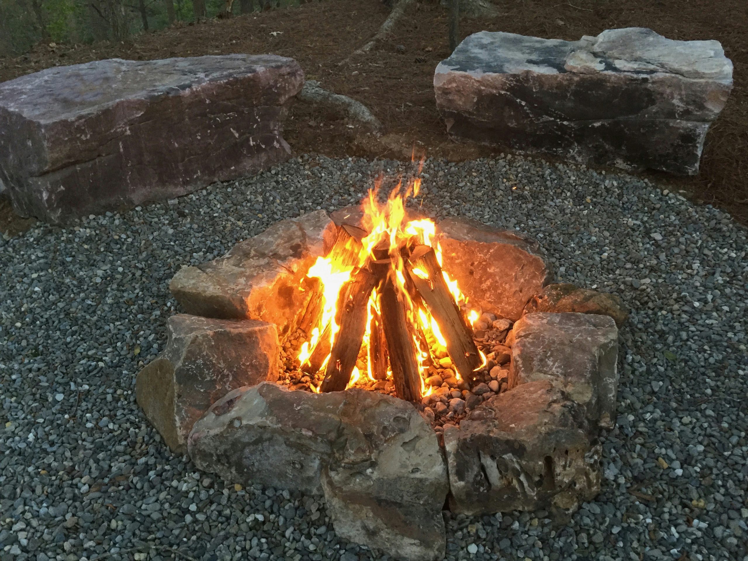 A nice fire in a fire pit made of natural stone boulders with boulders for benches in the background. North Carolina.