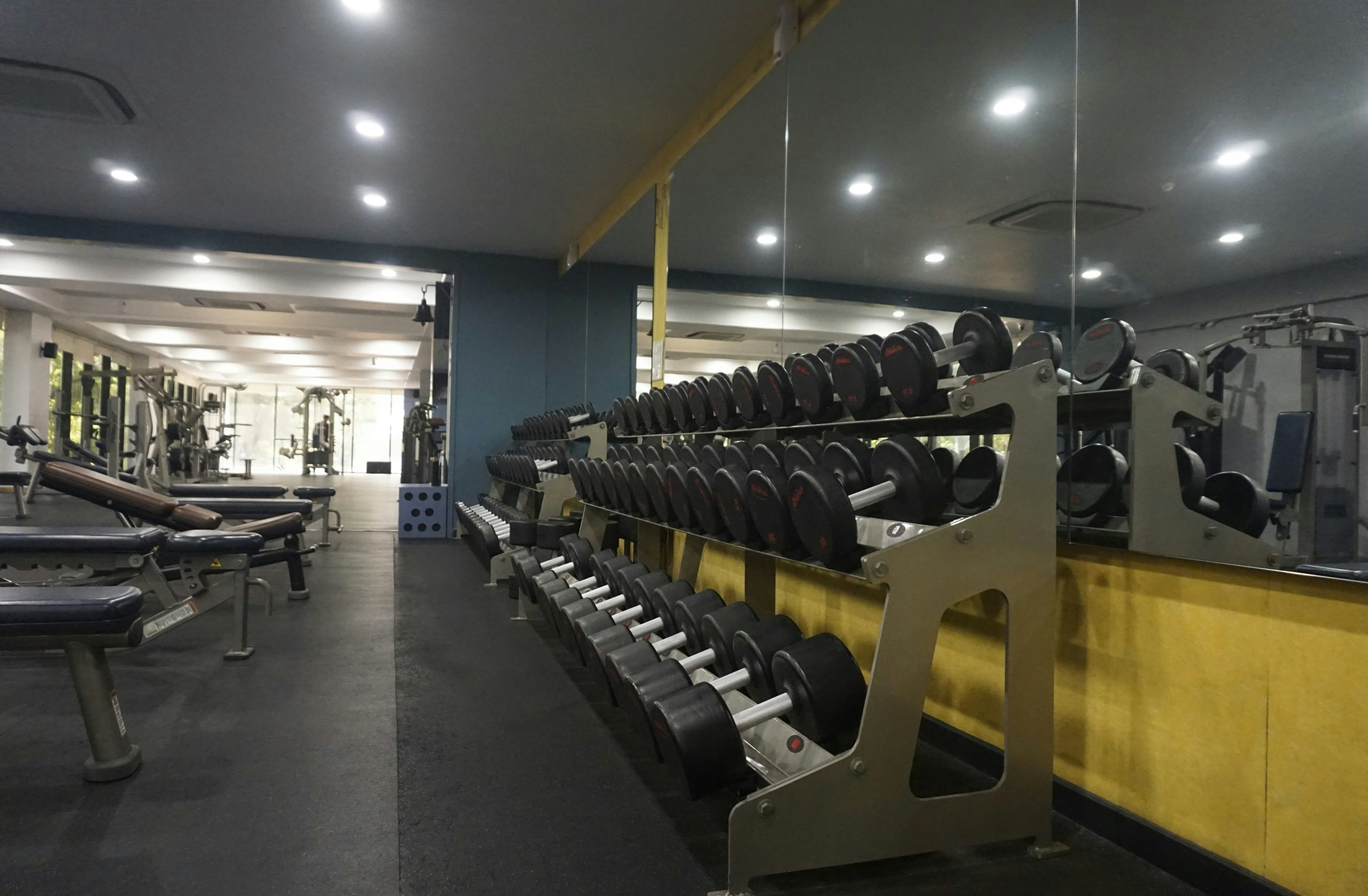 A perspective shot of a modern fitness facility showcasing a variety of strength training equipment and weight racks. The clean layout and bright, circular ceiling lights emphasize a well-organized an