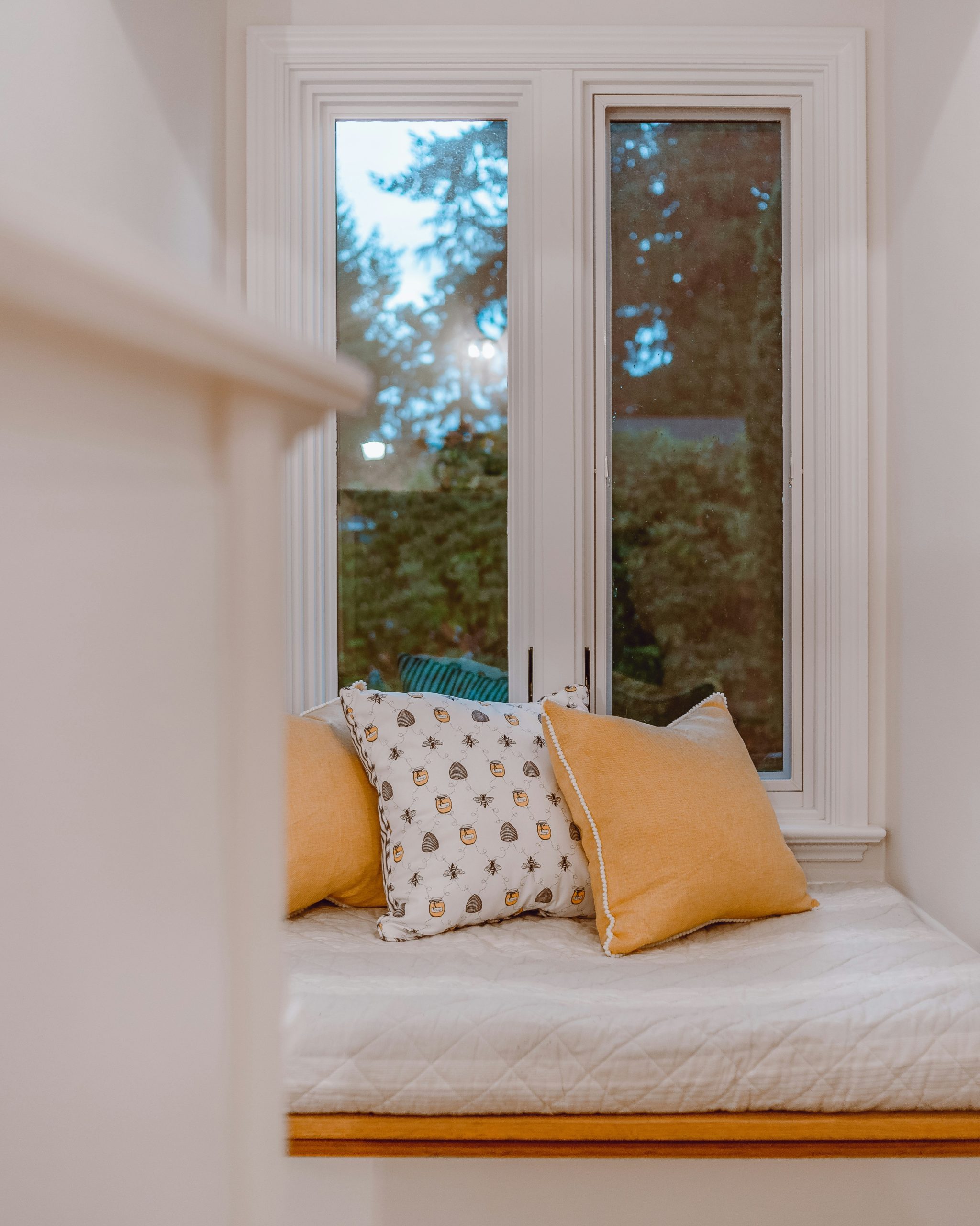 A quiet reading nook by the window on a white cushion with yellow pillows.