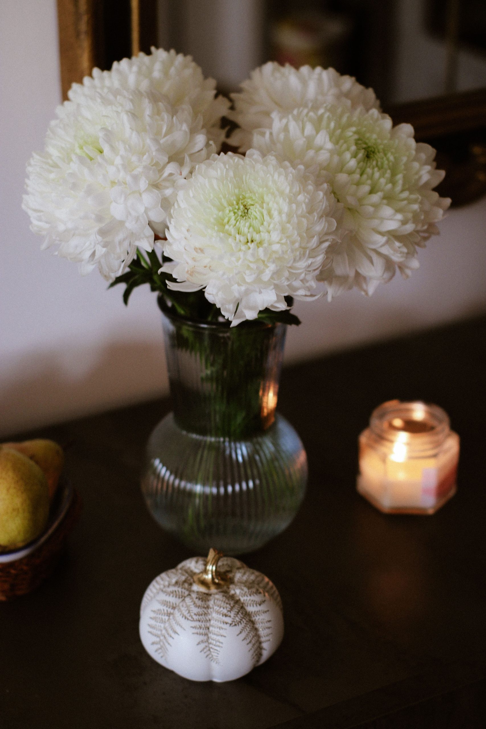 A serene composition featuring white chrysanthemums in a vase, pears, and a lit candle.