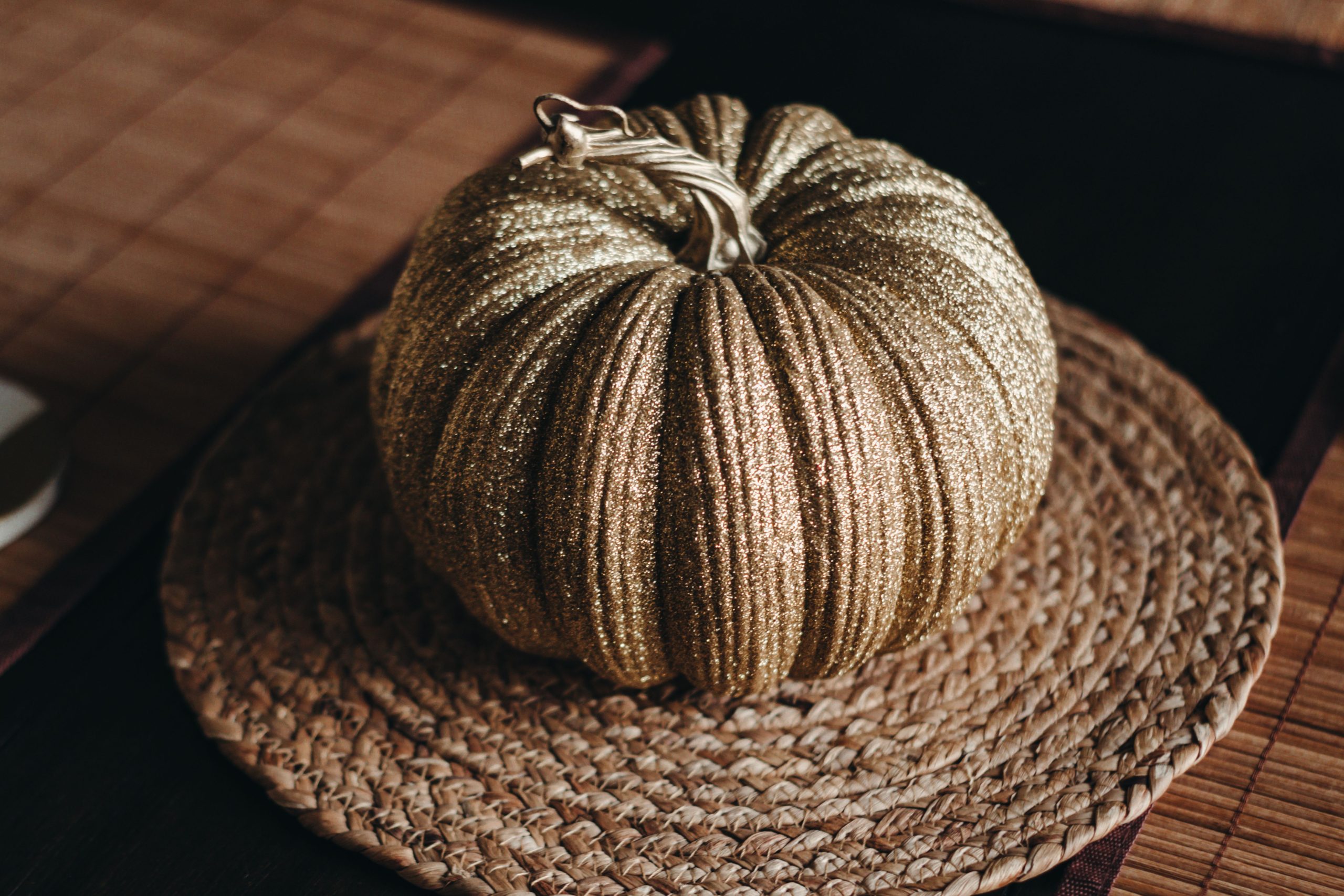 A shimmering gold pumpkin adorned with glitter sits elegantly on a woven mat, perfect for autumn décor.