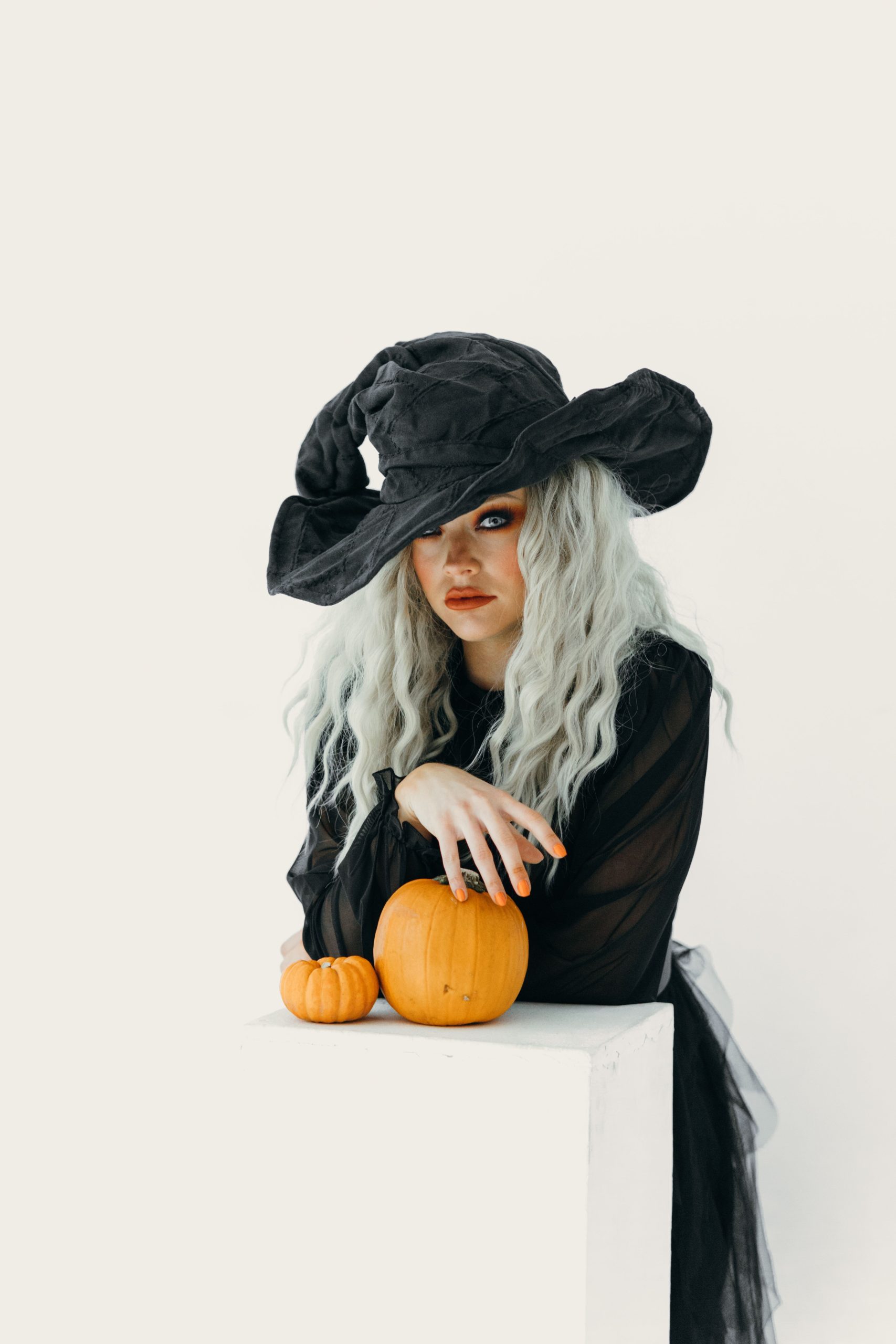 A stylish woman poses in a Halloween witch costume with pumpkins, embodying fall spirit.