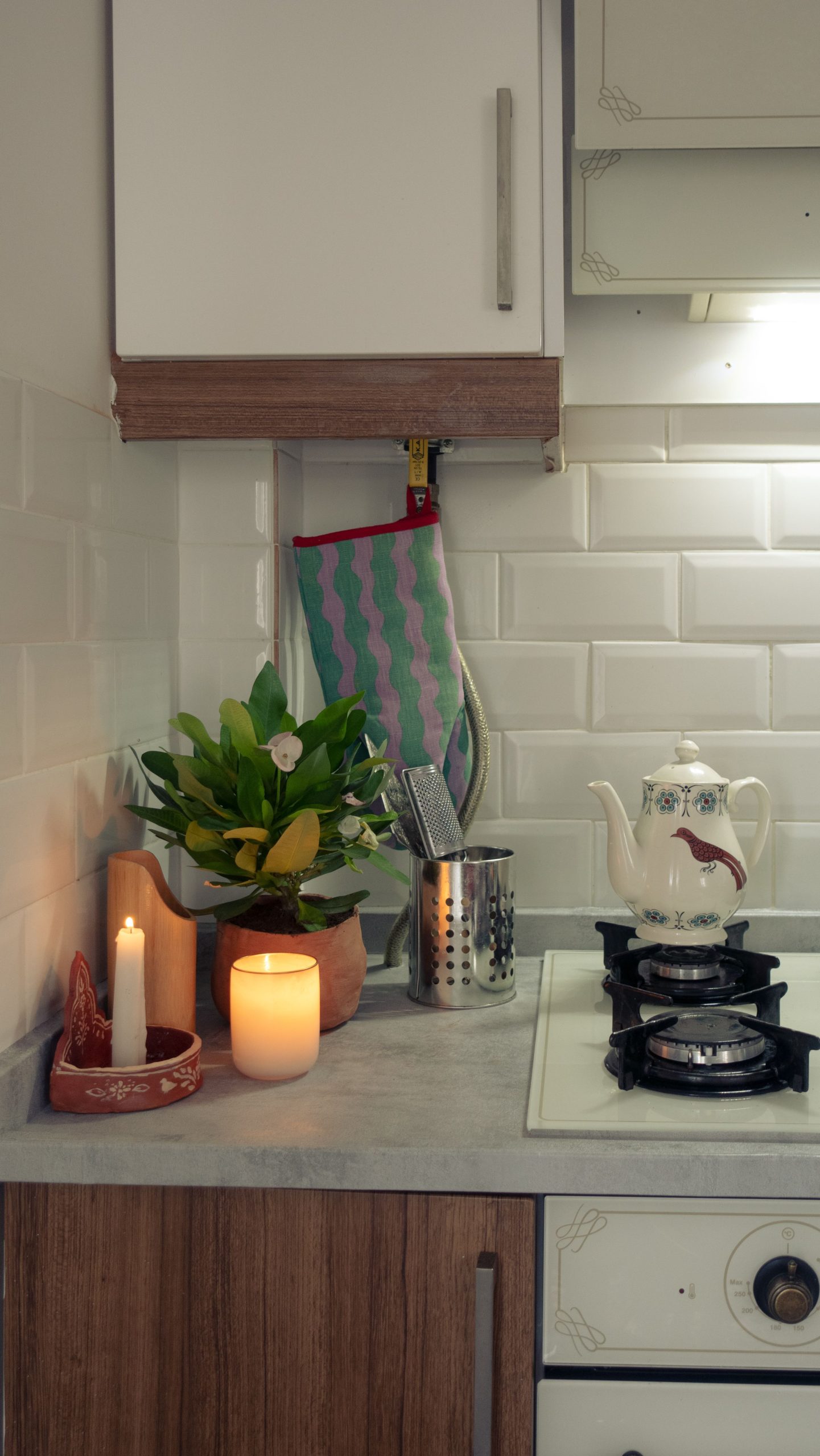 A warm and inviting kitchen counter with a teapot, candles, and potted plant for a cozy ambiance.