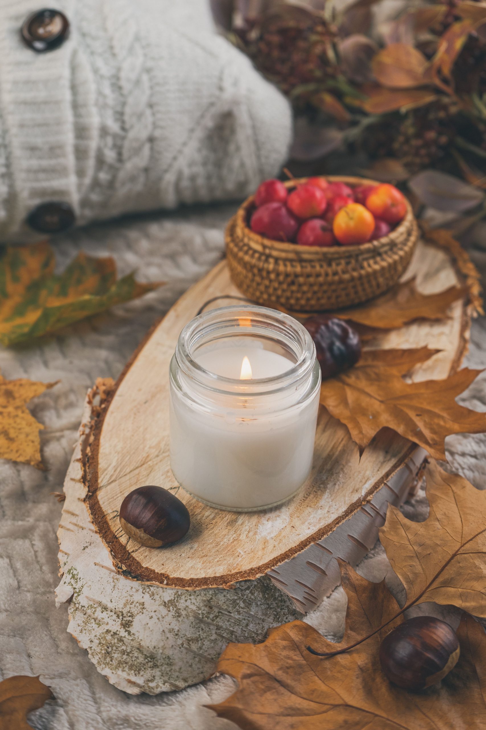 A warm, inviting autumn setup with a burning candle, chestnuts, and fall leaves.